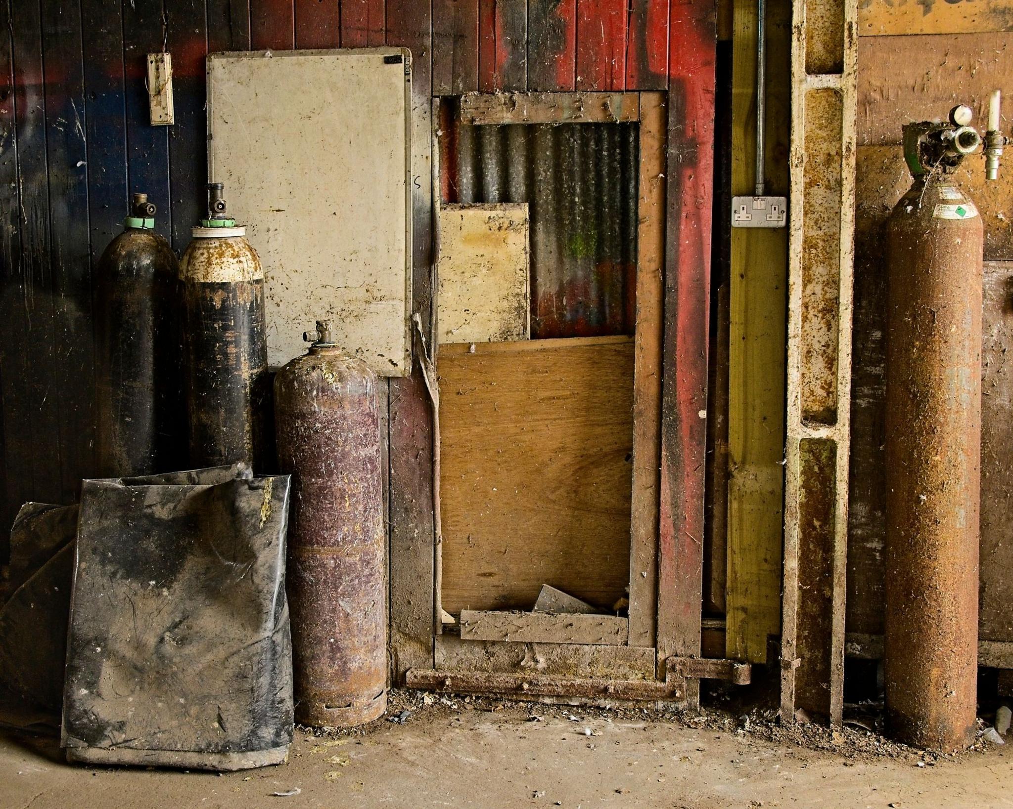 Disused rusty canisters lined up against a wall
