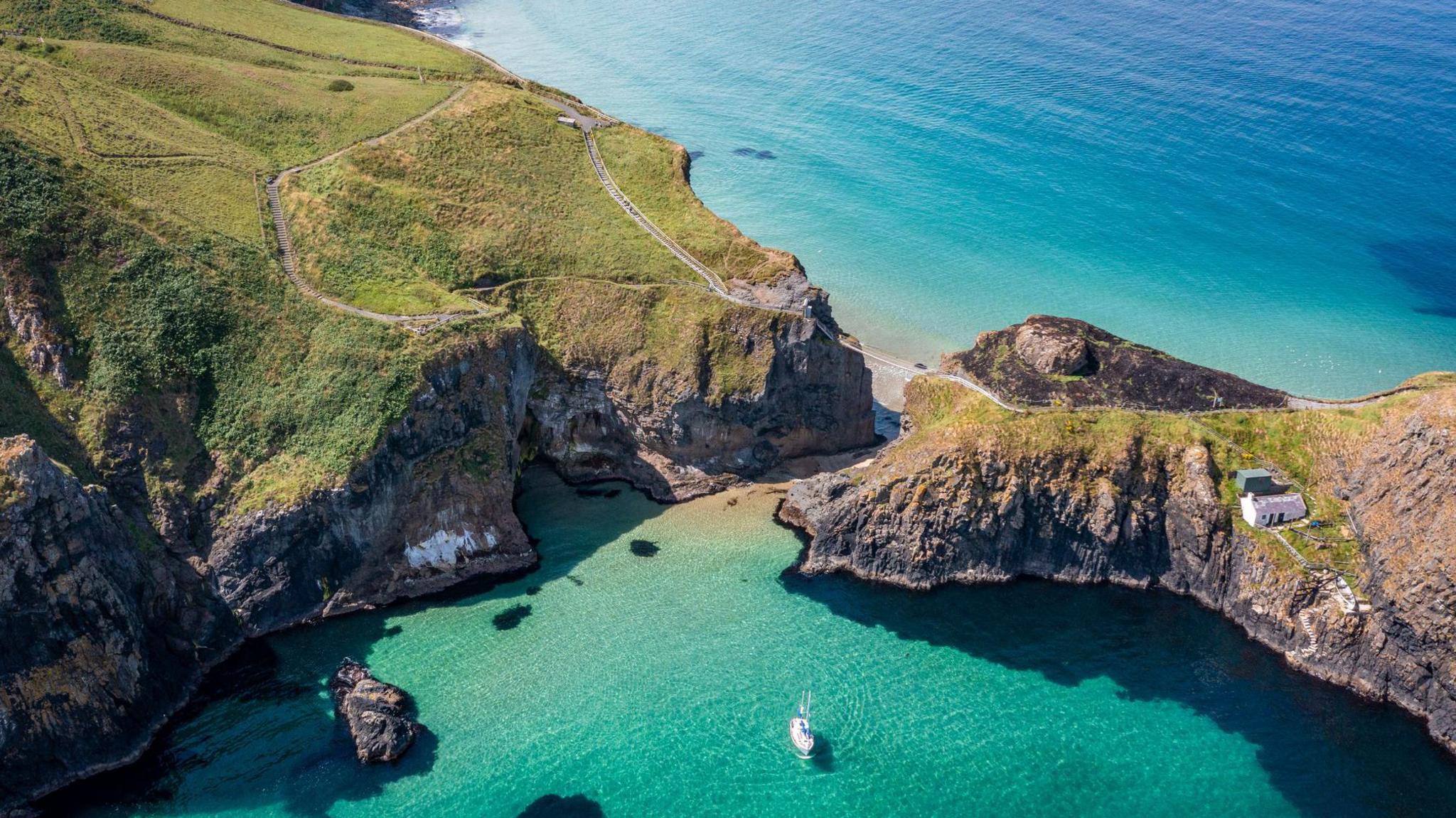 An aerial view of Carrick-a-Rede Rope Bridge. The sea is a beautiful blue colour. The bridge links the island to the mainland. It is a stock photo