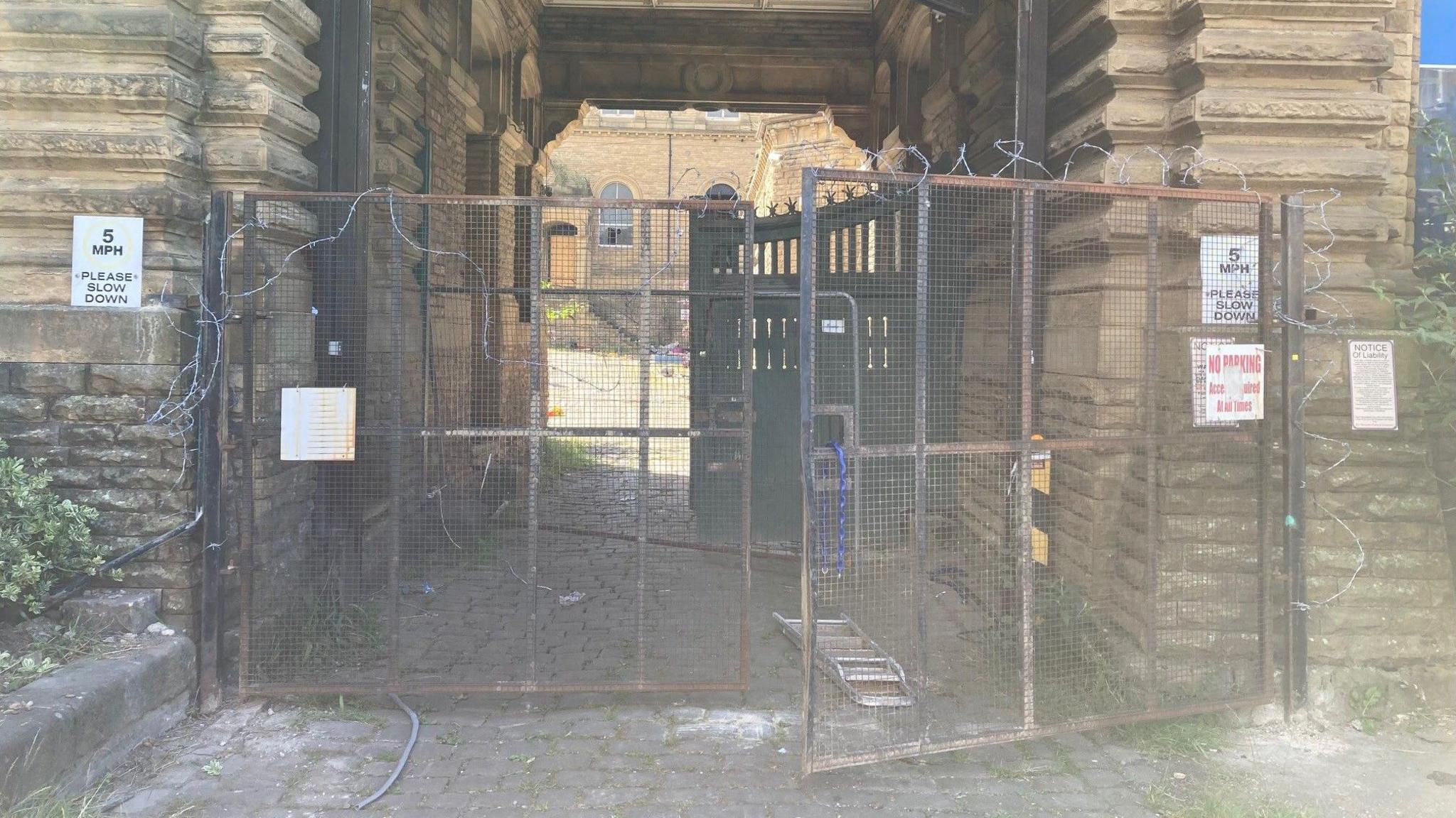 Gates with barbed wire on them lie open at the entrance into the mill complex