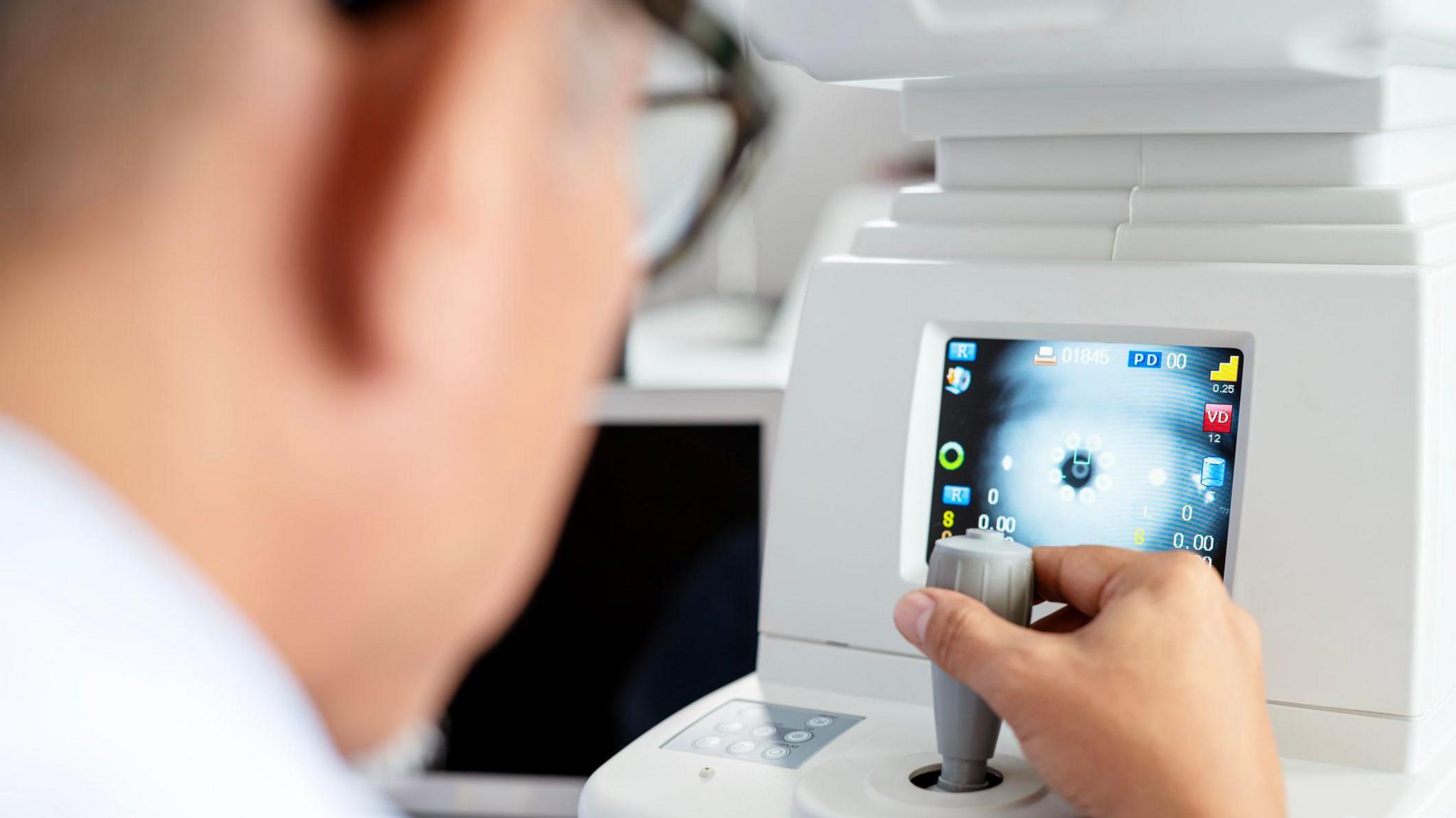Rear view of an ophthalmologist using a modern eye test equipment tool to perform a vision exam with his patient at an ophthalmologist's clinic.
