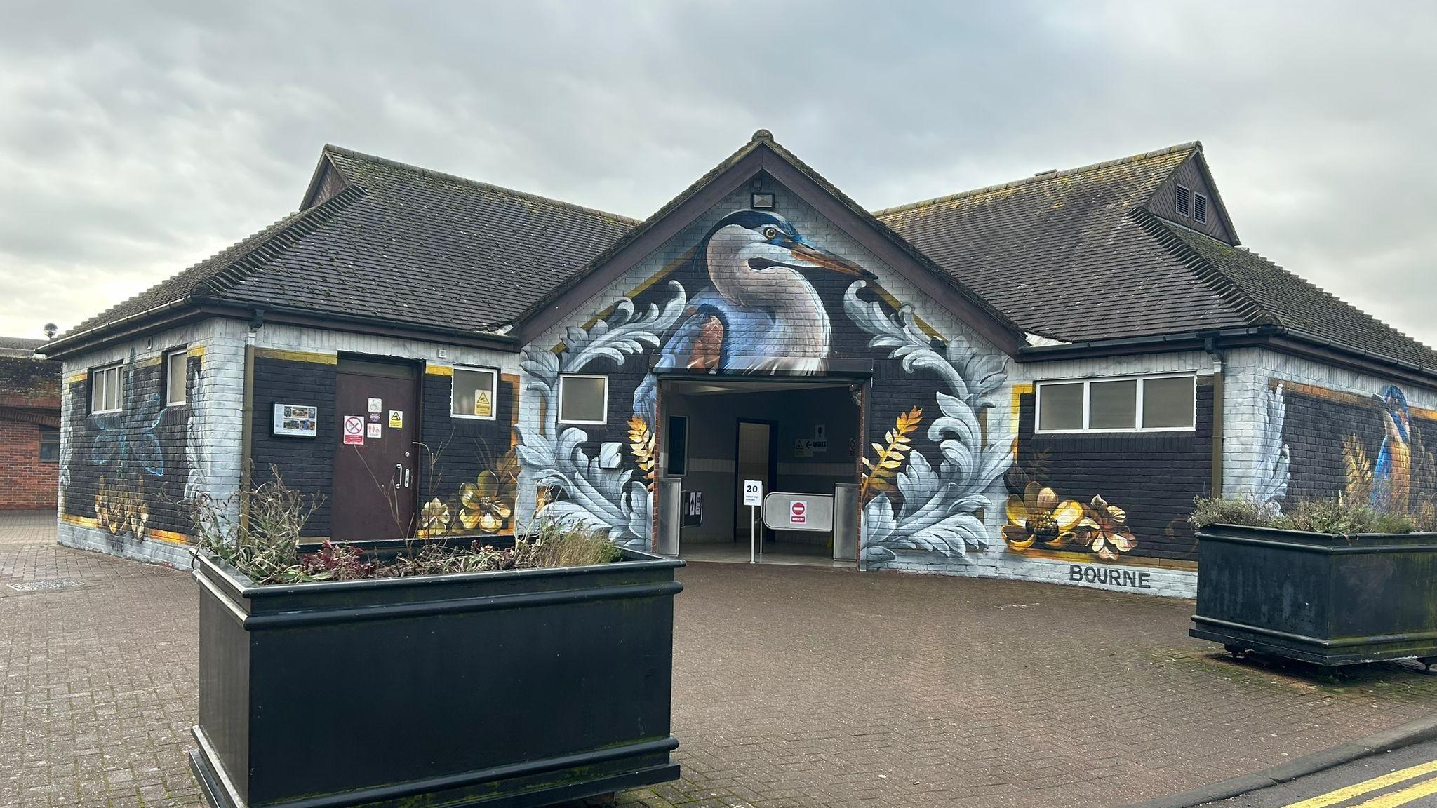 The outside of the Central Car Park toilet block in Salisbury. There is a bird and flowers painted on the building. 