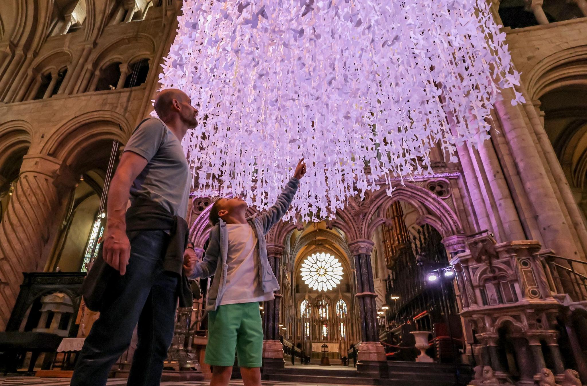 A boy points up at the thousands of white paper doves hung inside the cathedral as he stands with his father.