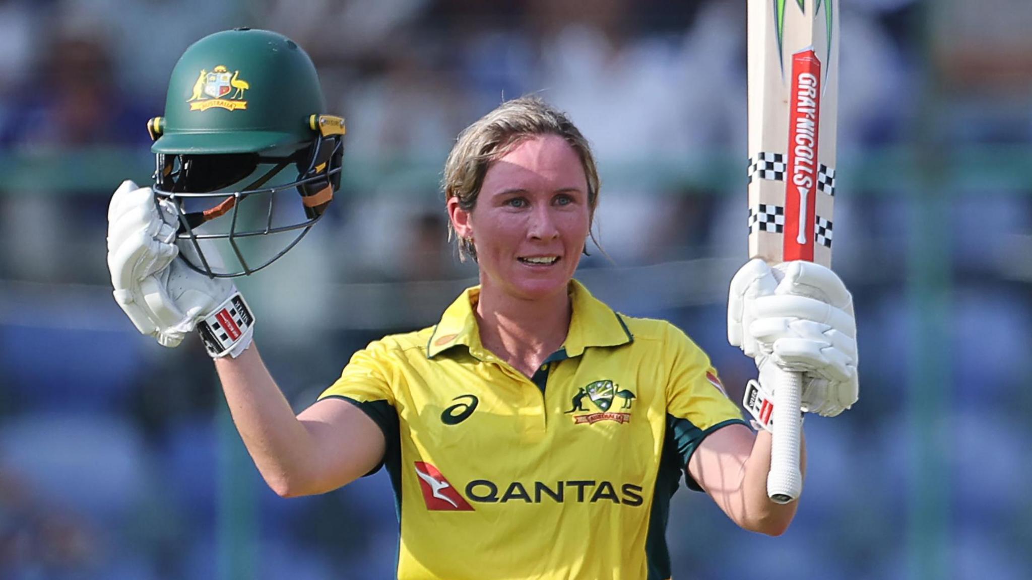 Australia batter Beth Mooney raises her helmet and bat to celebrate hitting a century against India in the third ODI