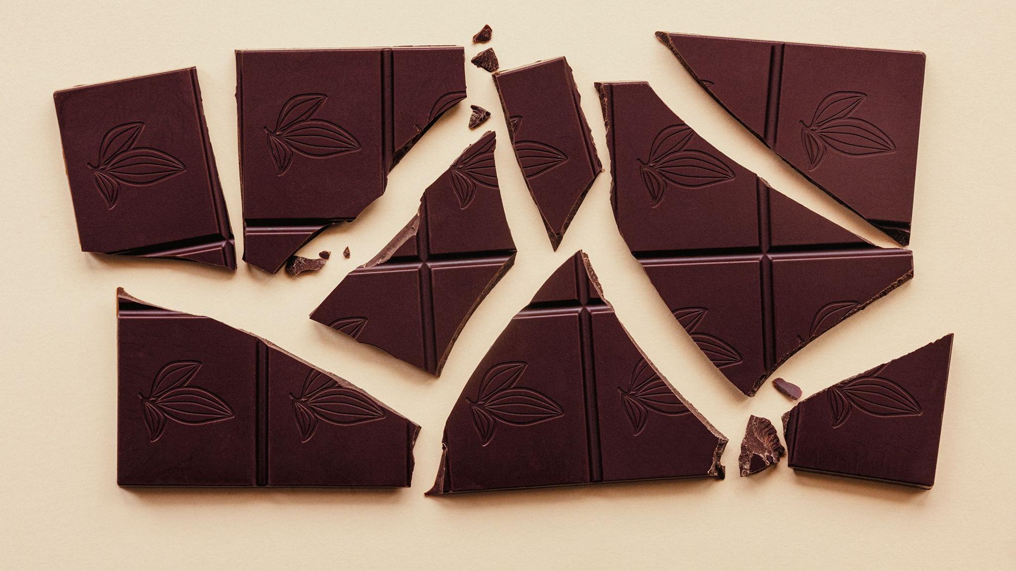 A dark chocolate bar broken into pieces on a beige background