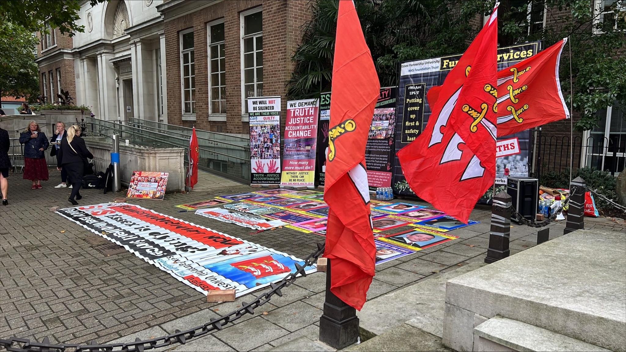 Placards and posters outside the Civic Centre in Chelmsford. They are mostly accusing the Essex Partnership University NHS Foundation Trust of causing the deaths of people. They are black with colourful font.