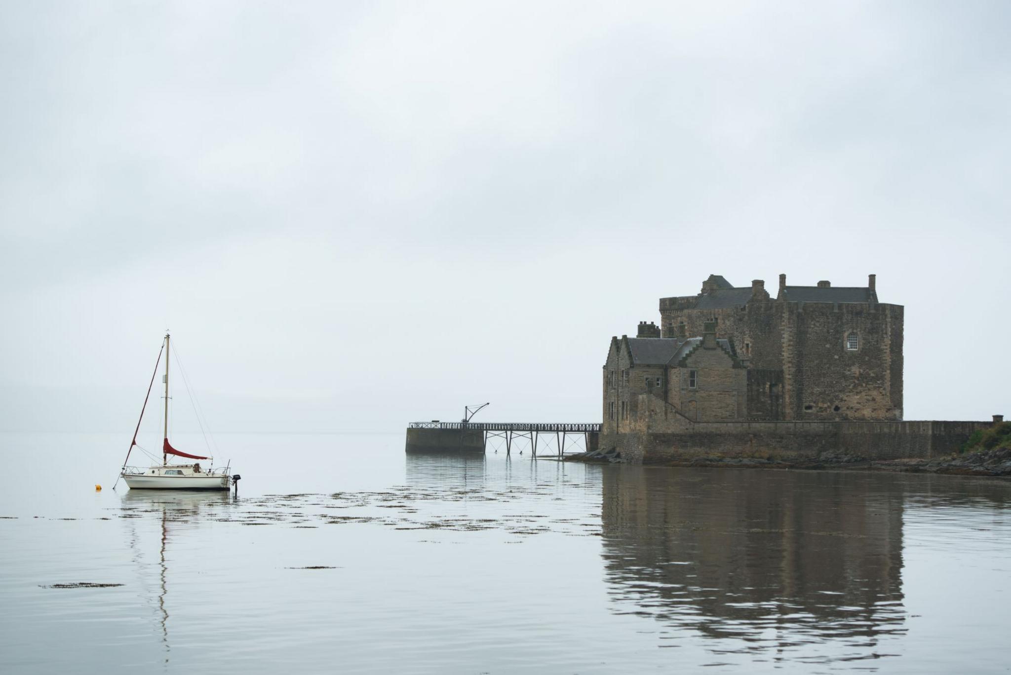 Landscape of a boat in the water with a castle in the background on a foggy day