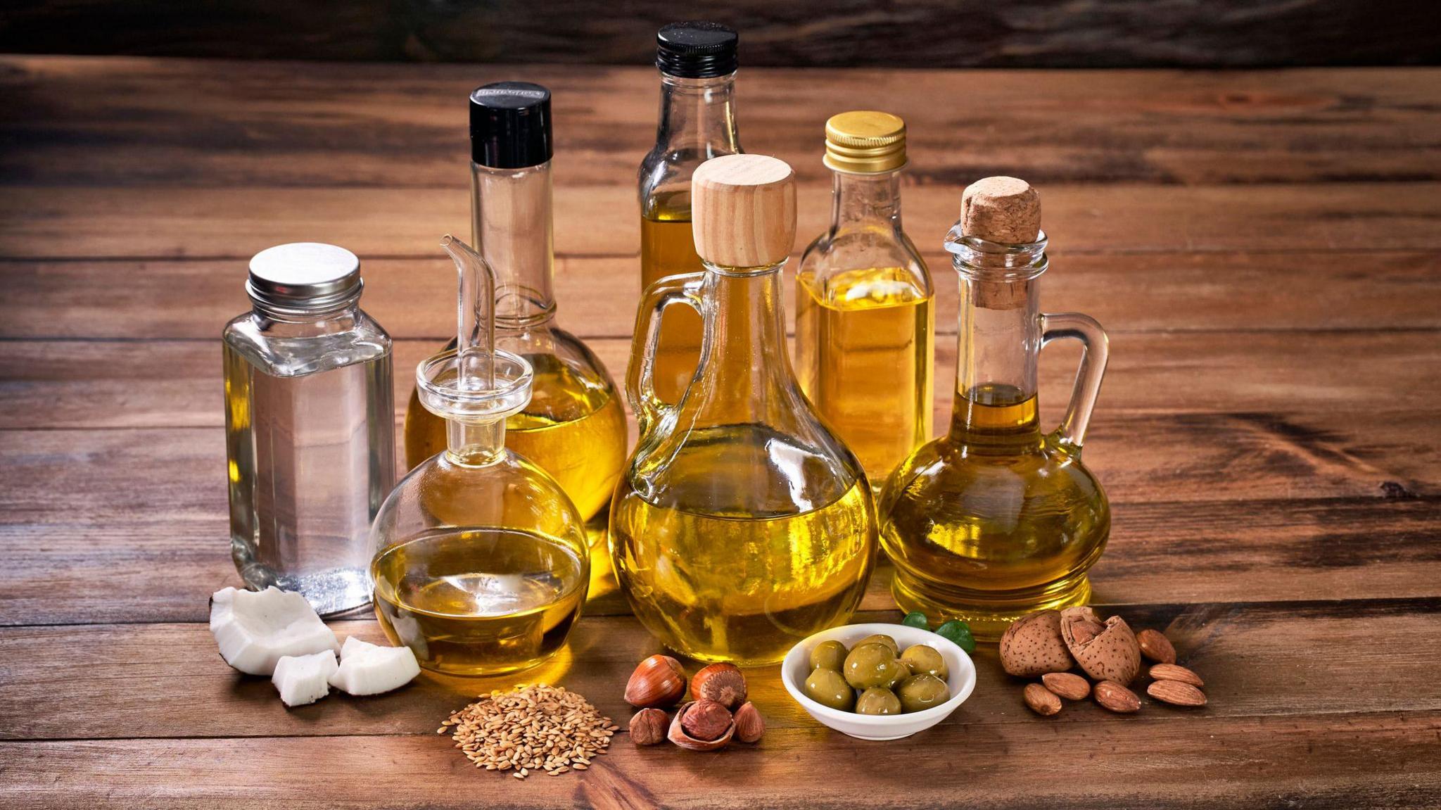 Assorted healthy vegetable oil bottle collection on wooden table in a old fashioned kitchen with low key illumination: Olive oil, hazelnut oil, almond oil, coconut oil and sesame oil
