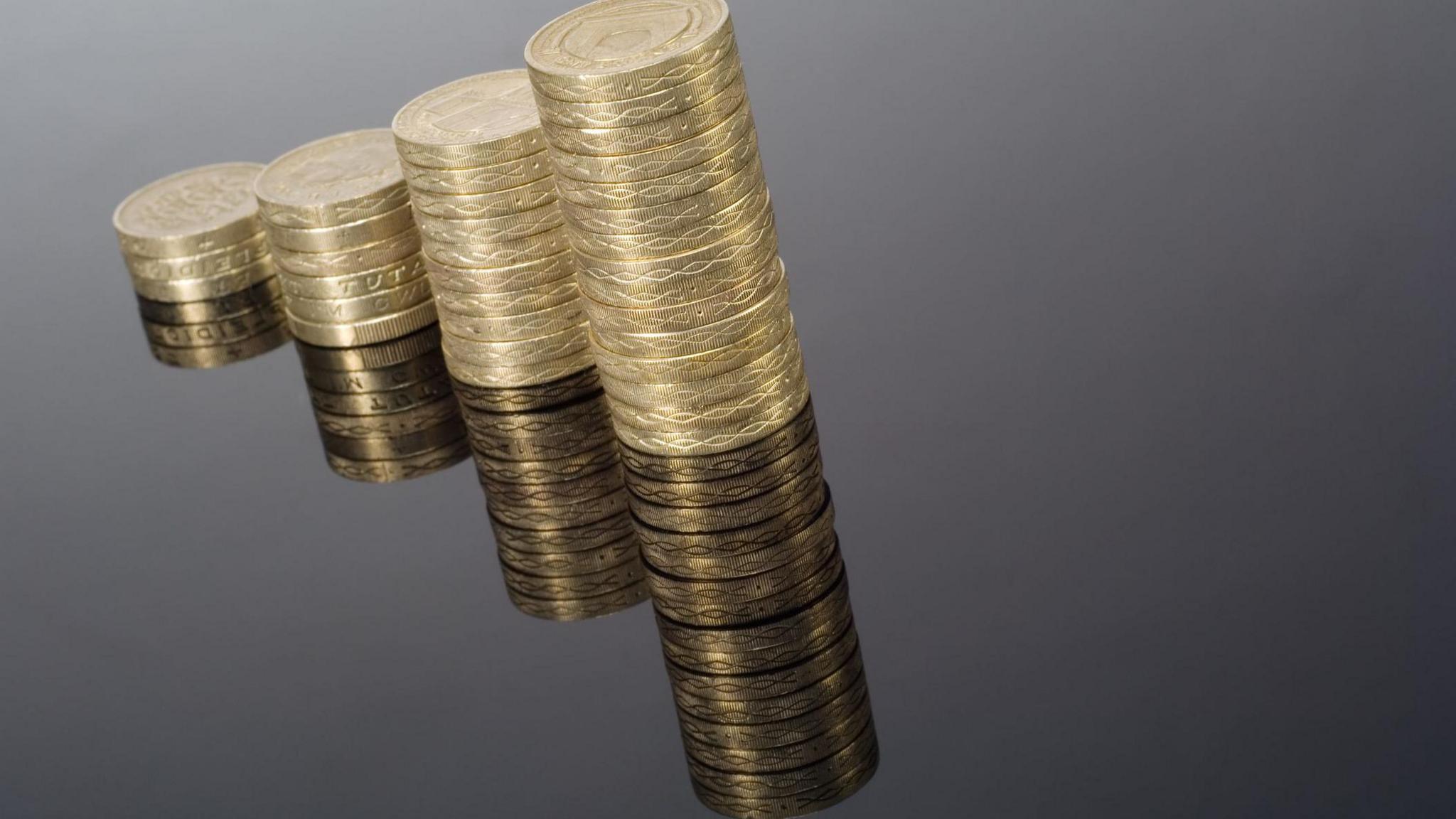 Pound coin graphic with columns on black - stock photo. The four piles of coins are stacked taller as you move from left to right. They are also reflected with a mirror effect in the bottom half of the picture. 