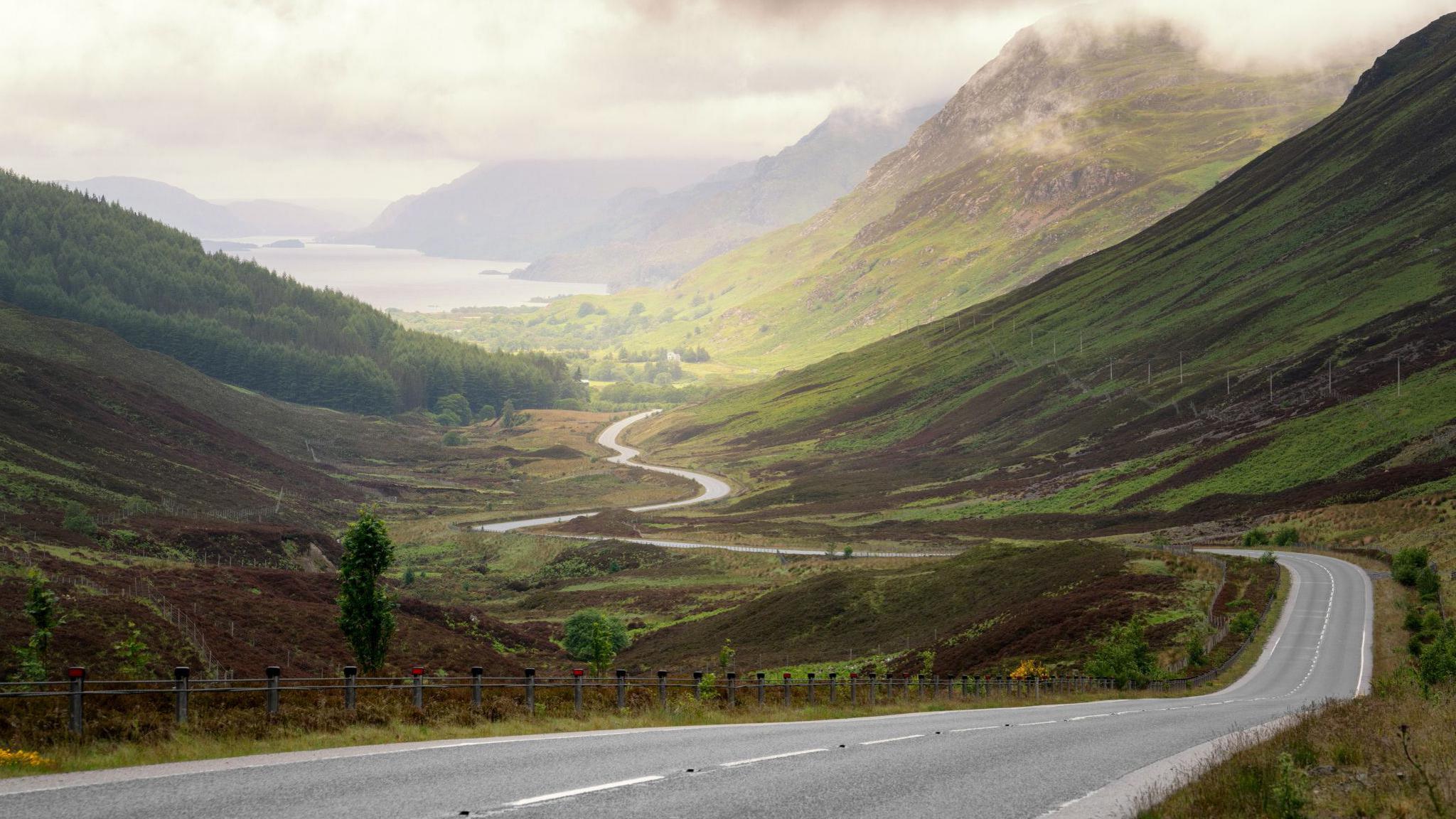 A road in the Scottish Highlands with a loch in the distance