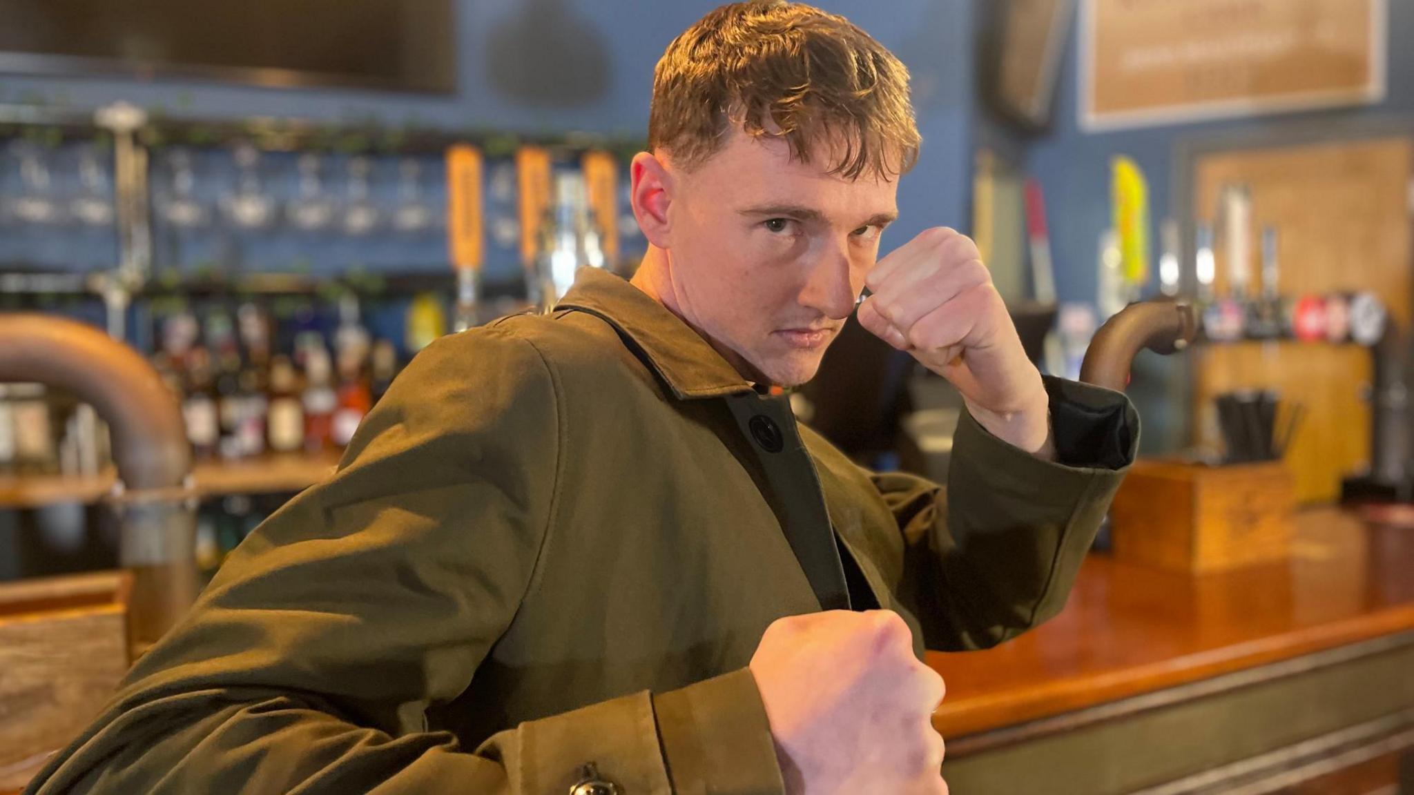 A young man in closely cropped hair clenches his fists up to the camera