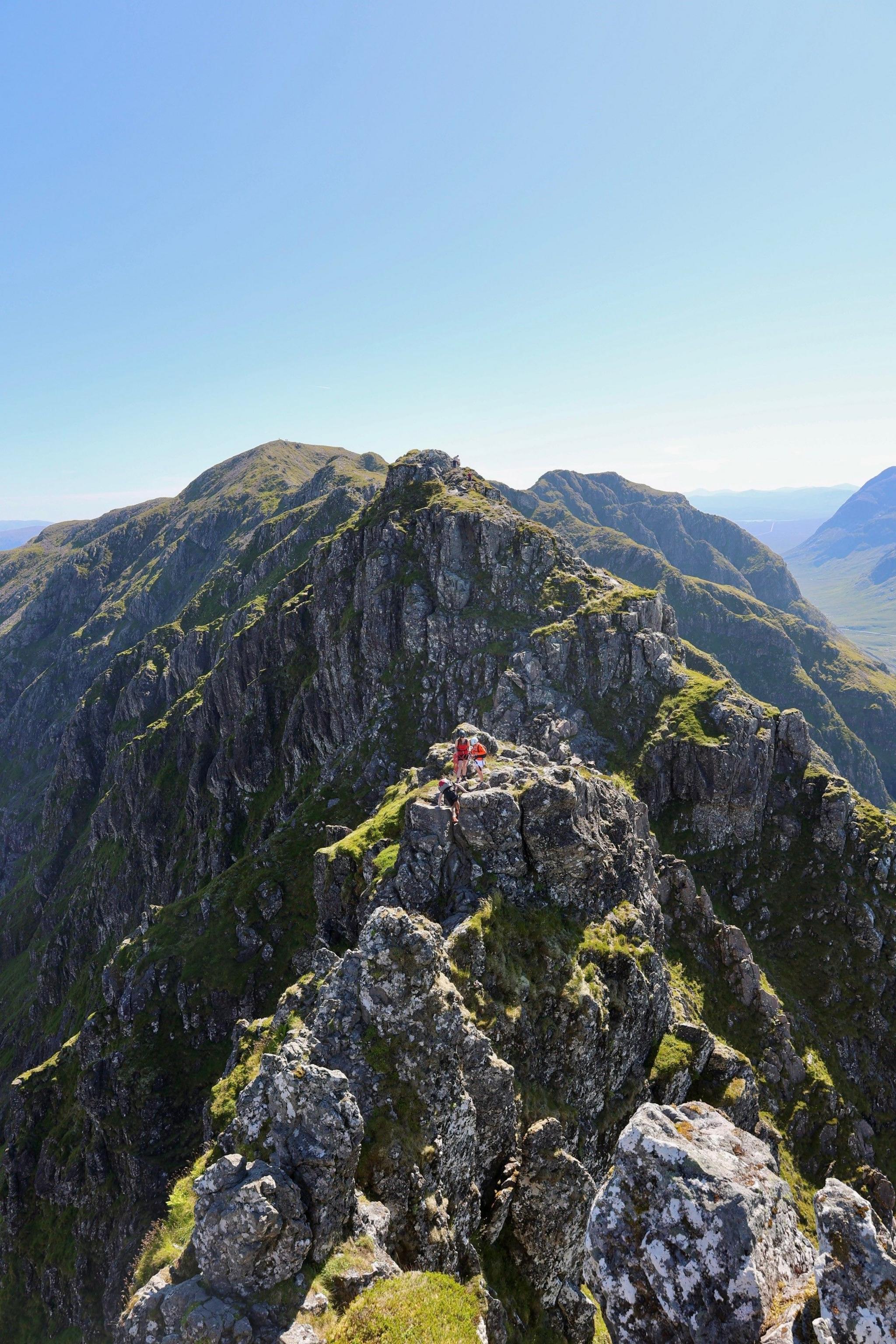 A rocky outcrop of jagged rock along the ridge of a mountain with climbers on top.