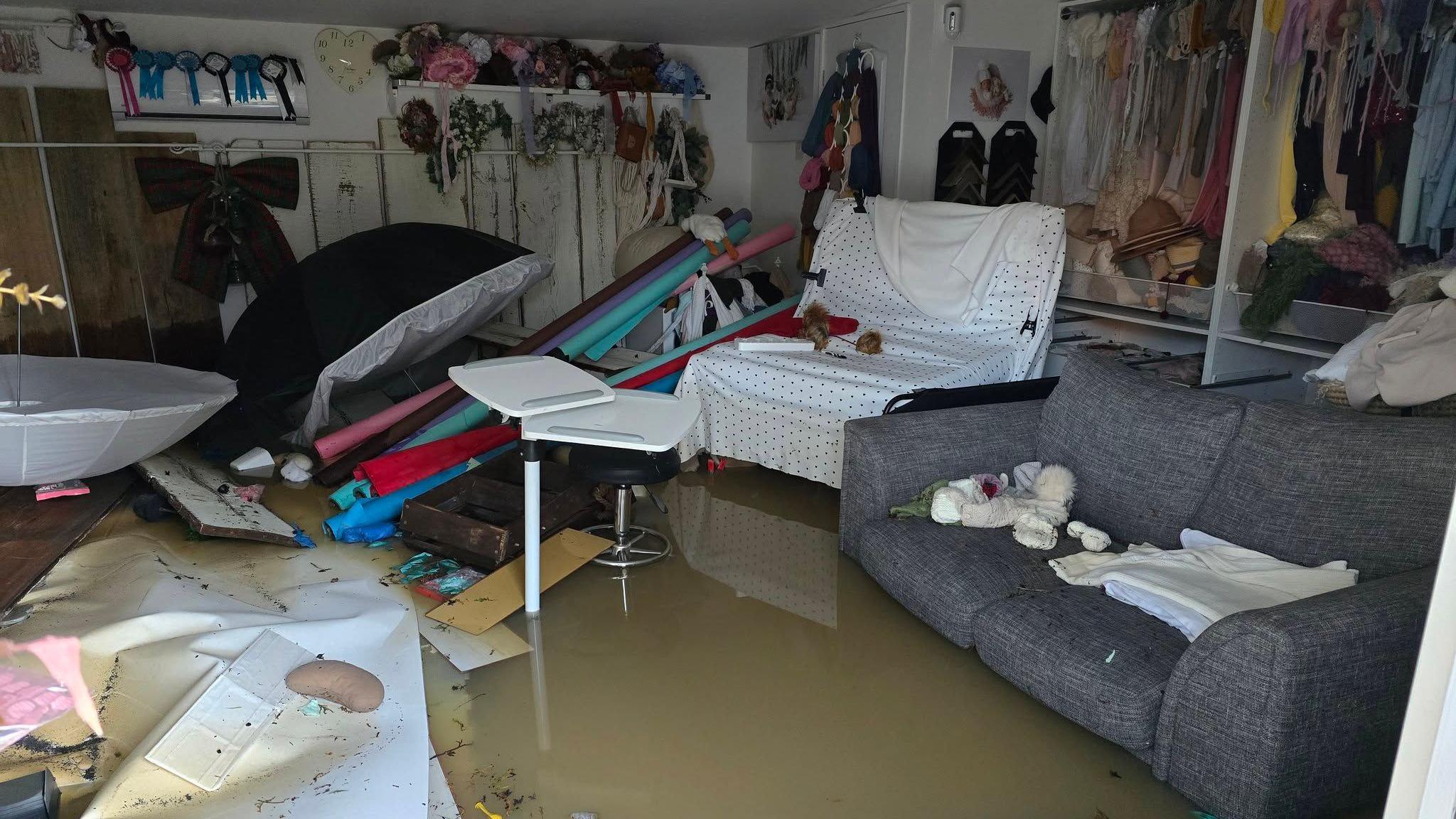 An image of a flooded room with a sofa and chair covered in a polka dot fabric with materials and unidentifiable equipment engulfed in water