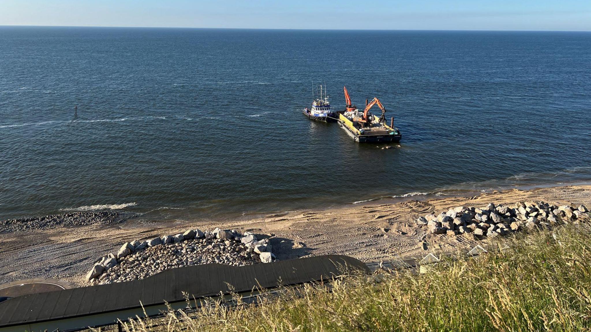 Rock groins on a beach with barge and pontoon in sea