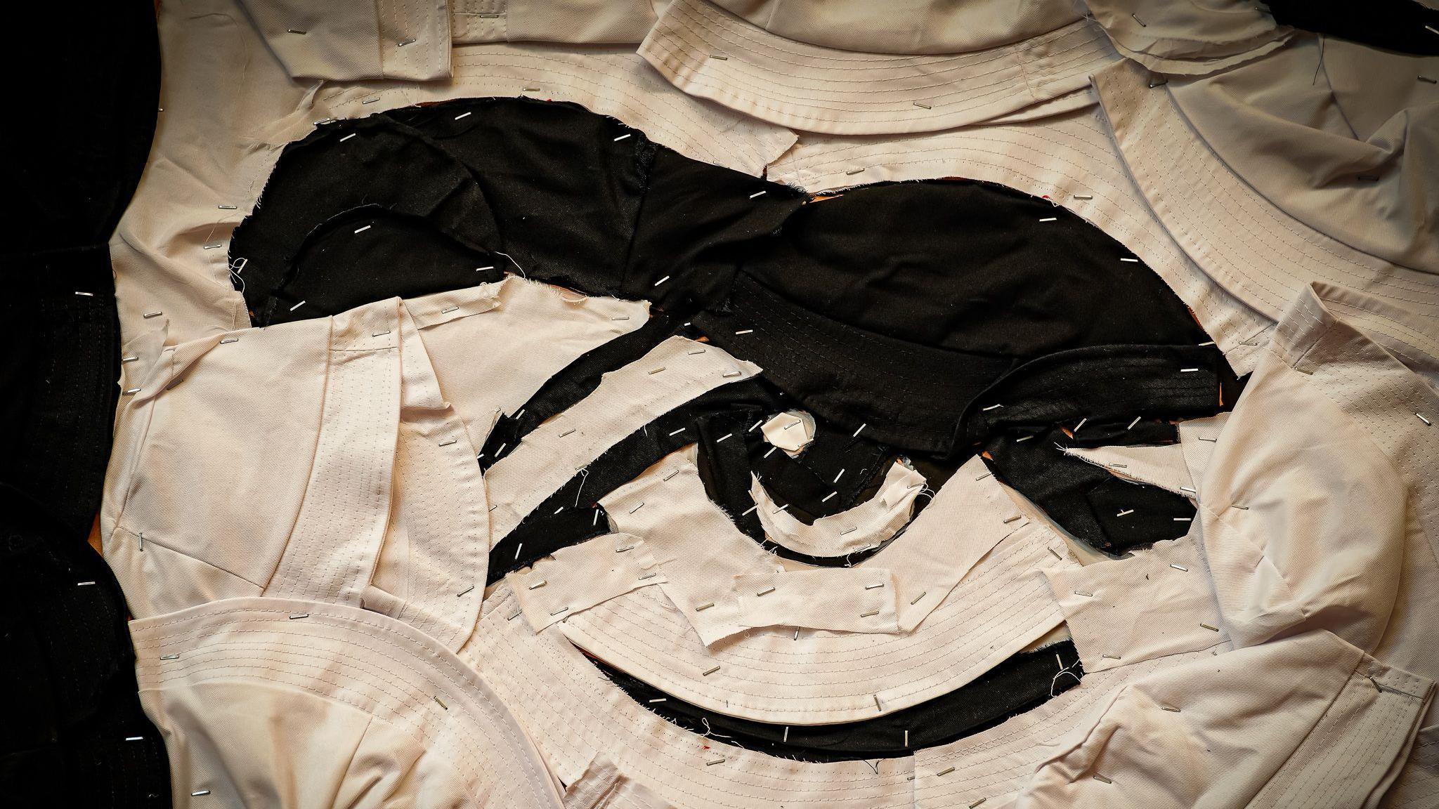 A an extreme close up of the mural shows the how the hats are stapled together with bit of a black showing through the white to make the shape of the image. some of the hats are in tact but on the eye and eye brow it looks like some of the hats have been cut up. 
