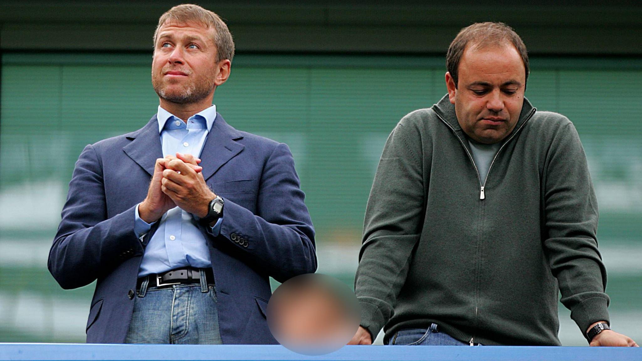 Roman Abramovich and Eugene Shvidler standing next to each other. Mr Abramovich is wearing a blue blazer over jeans and has his hands clasped together as he looks into the distance. Mr Shvidler is wearing a quarter-zip jumper in green and is leaning on the railing, looking downwards with a resigned expression