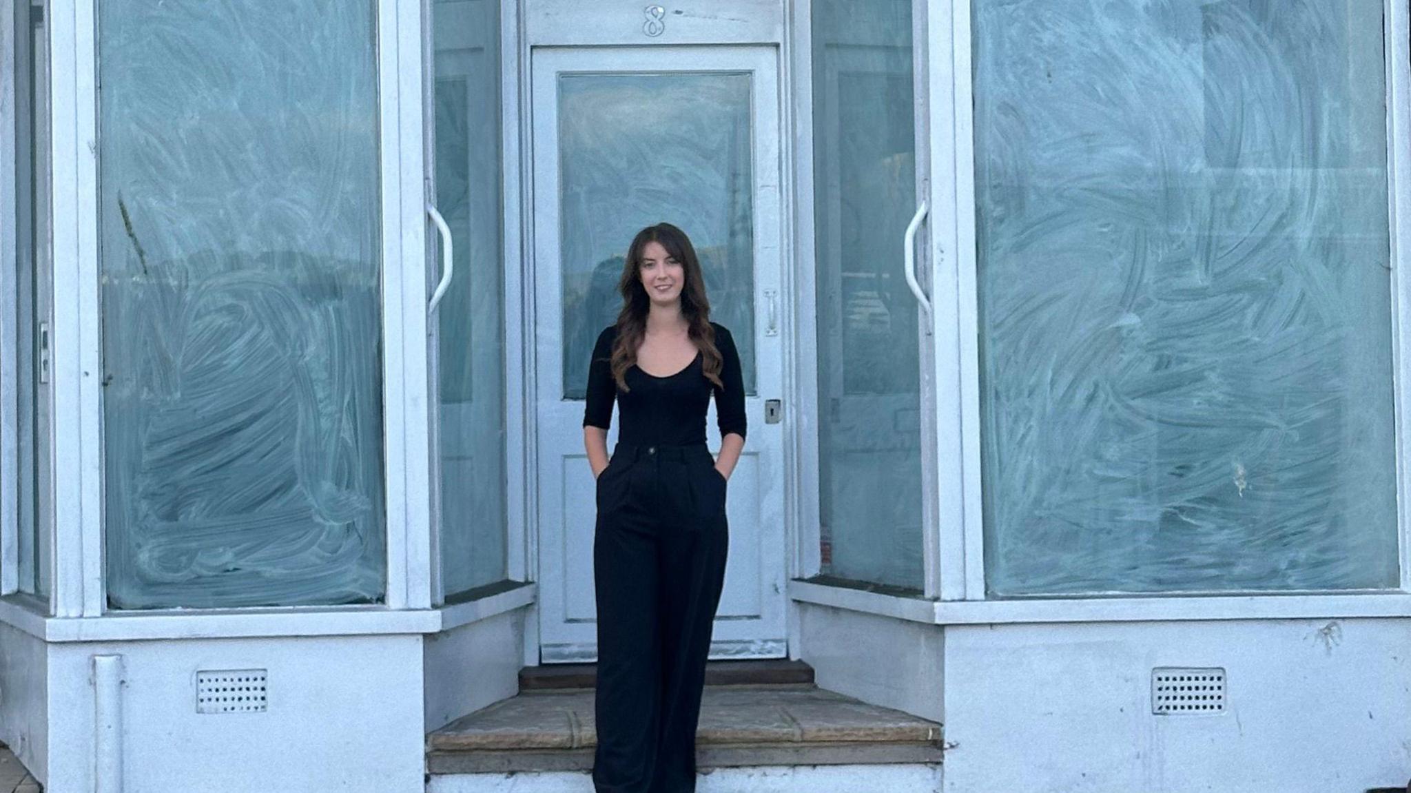 Naomi Woods outside a vacant shop, which currently has windows painted over in white. The door and frames of the large windows are also painted white.