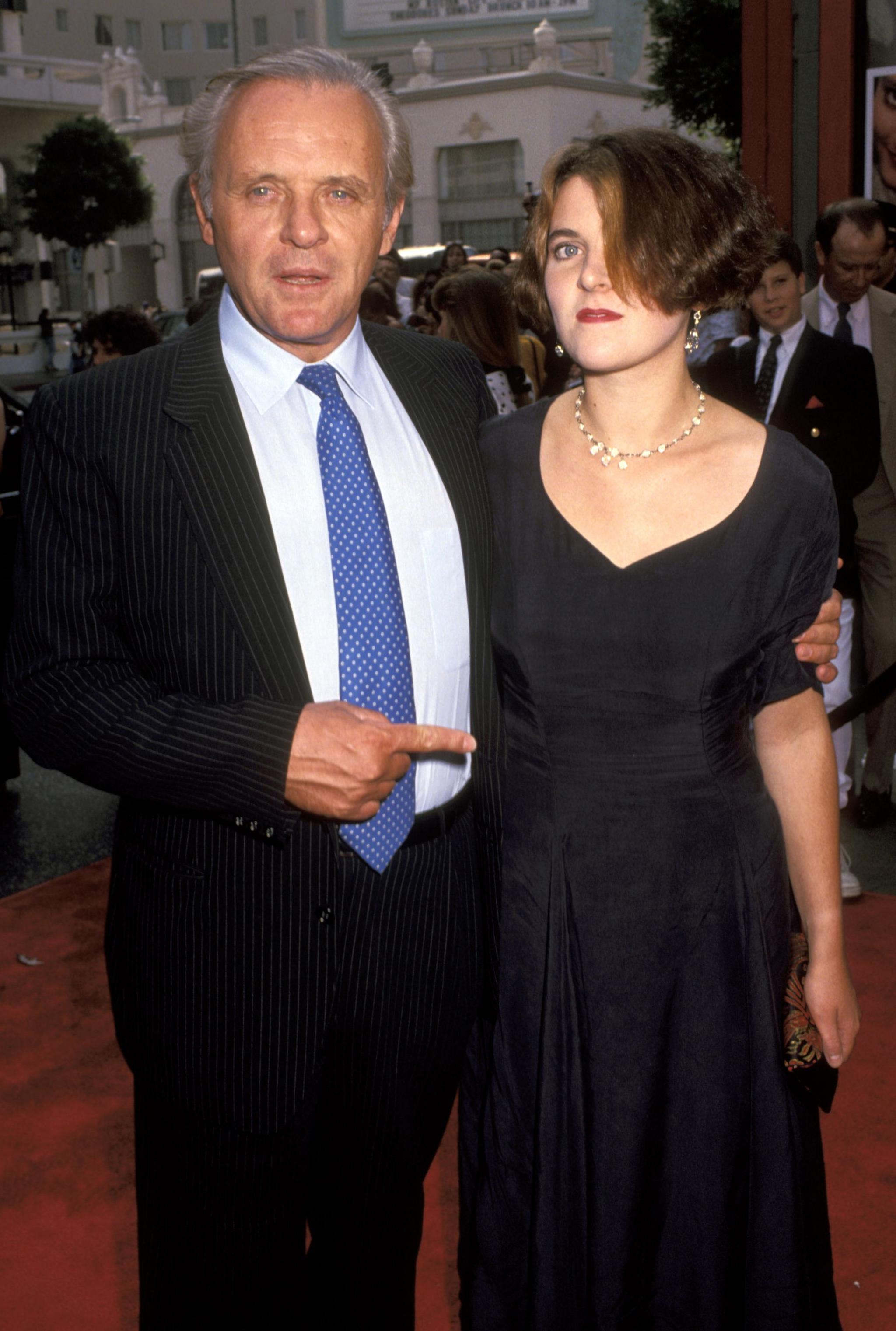 Hopkins in black suit, white shirt and blue tie, with his arm around his daughter Abigail, short bob,  in black dress and gold necklace. Hopkins is pointing to her