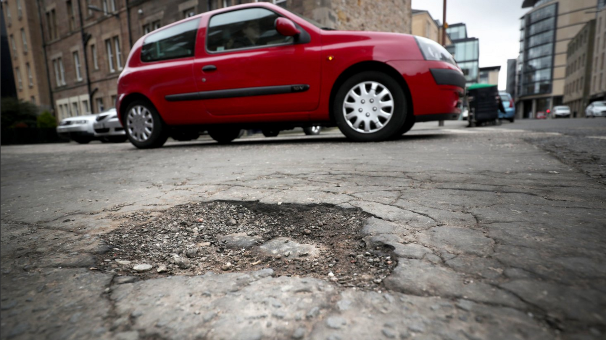 A pothole in an urban road with a red car behind