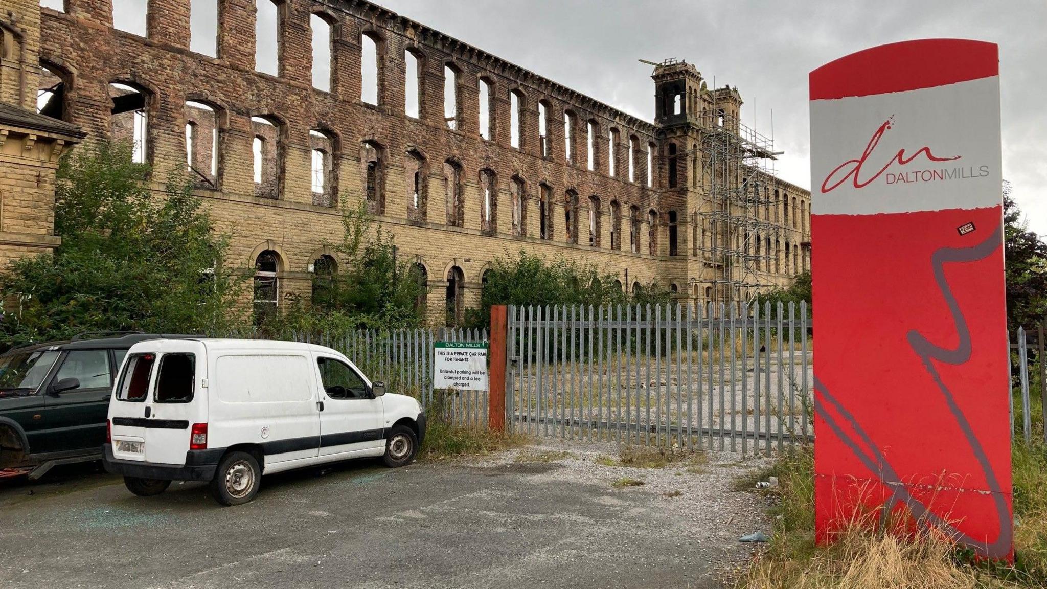 Two smashed up vehicles parked outside the burnt-out main building of the Dalton Mills complex