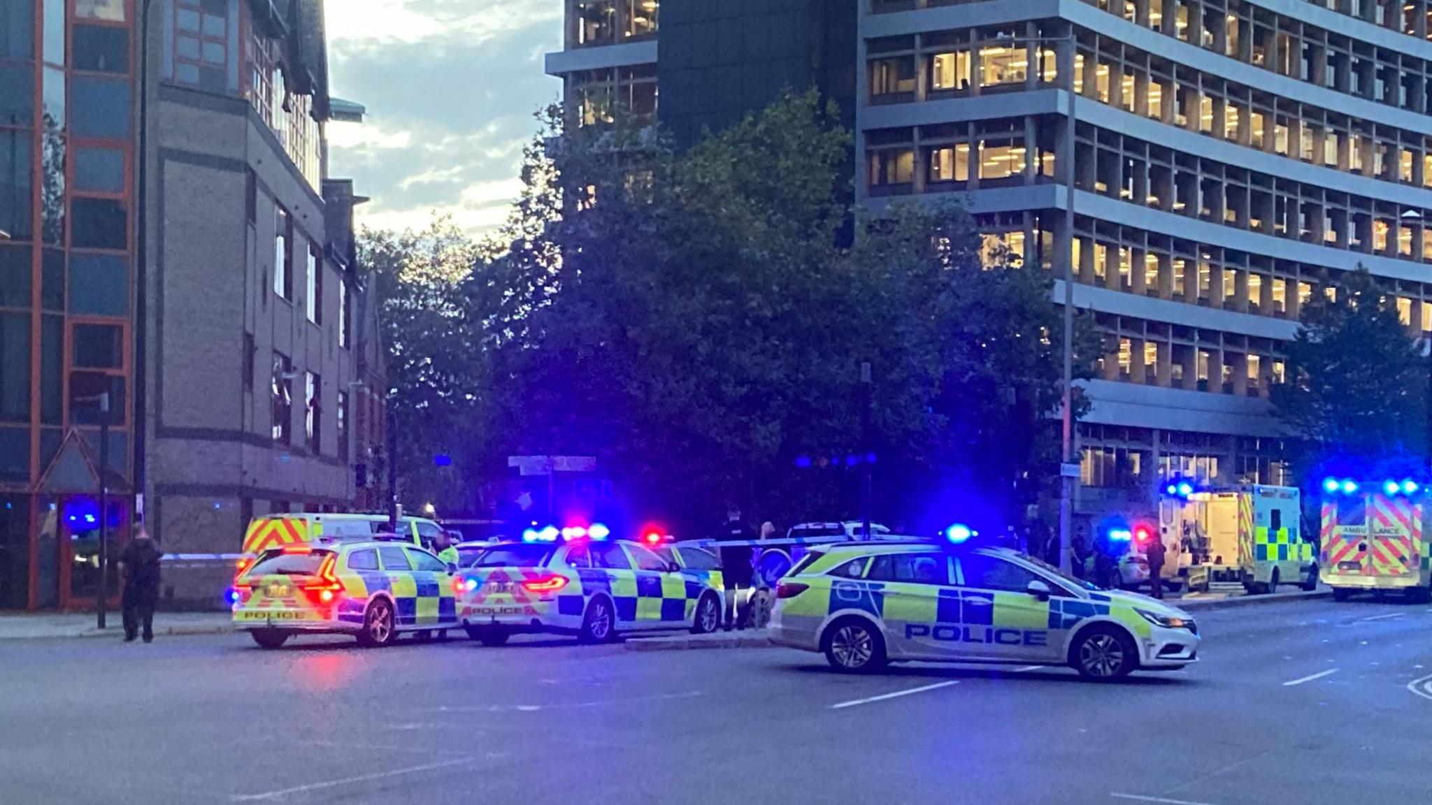 Several police vehicles and ambulances blocking off traffic heading north from the Civic Drive/Princes Street crossroads in Ipswich. The curved AXA building and other offices, including the Ipswich Buddhist Centre, are in the background