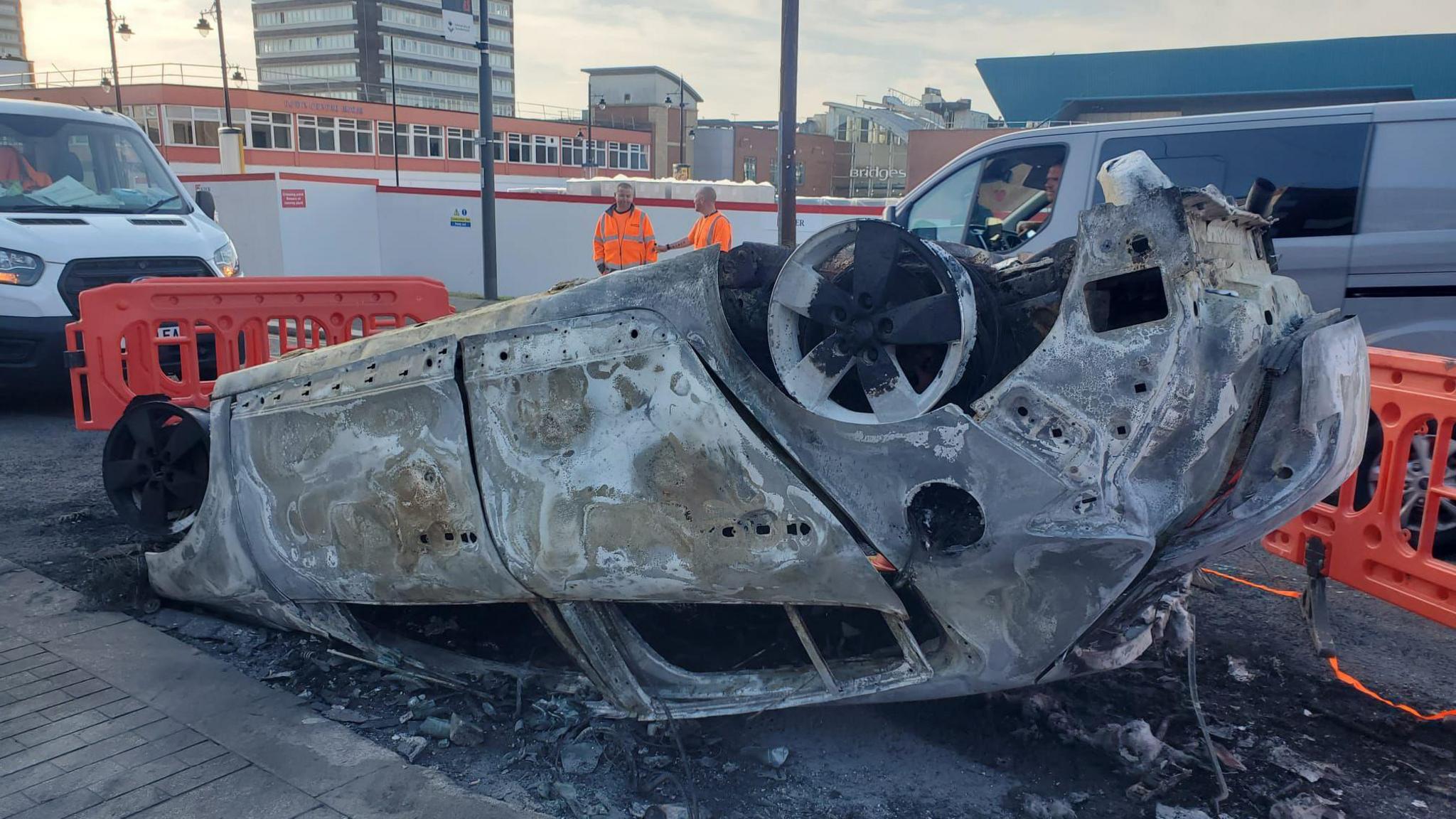 A burnt out shell of a police car on its roof.