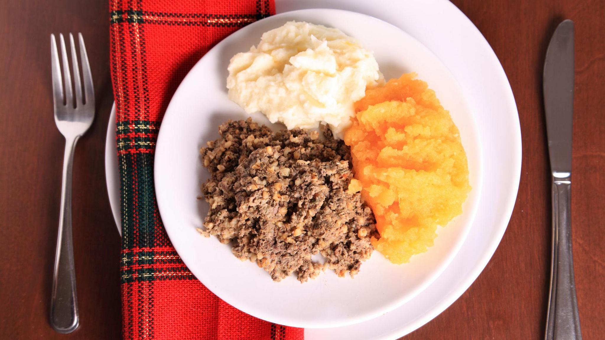 Haggis, neeps and tatties on a white plate with a red and green tartan napkin next to it.