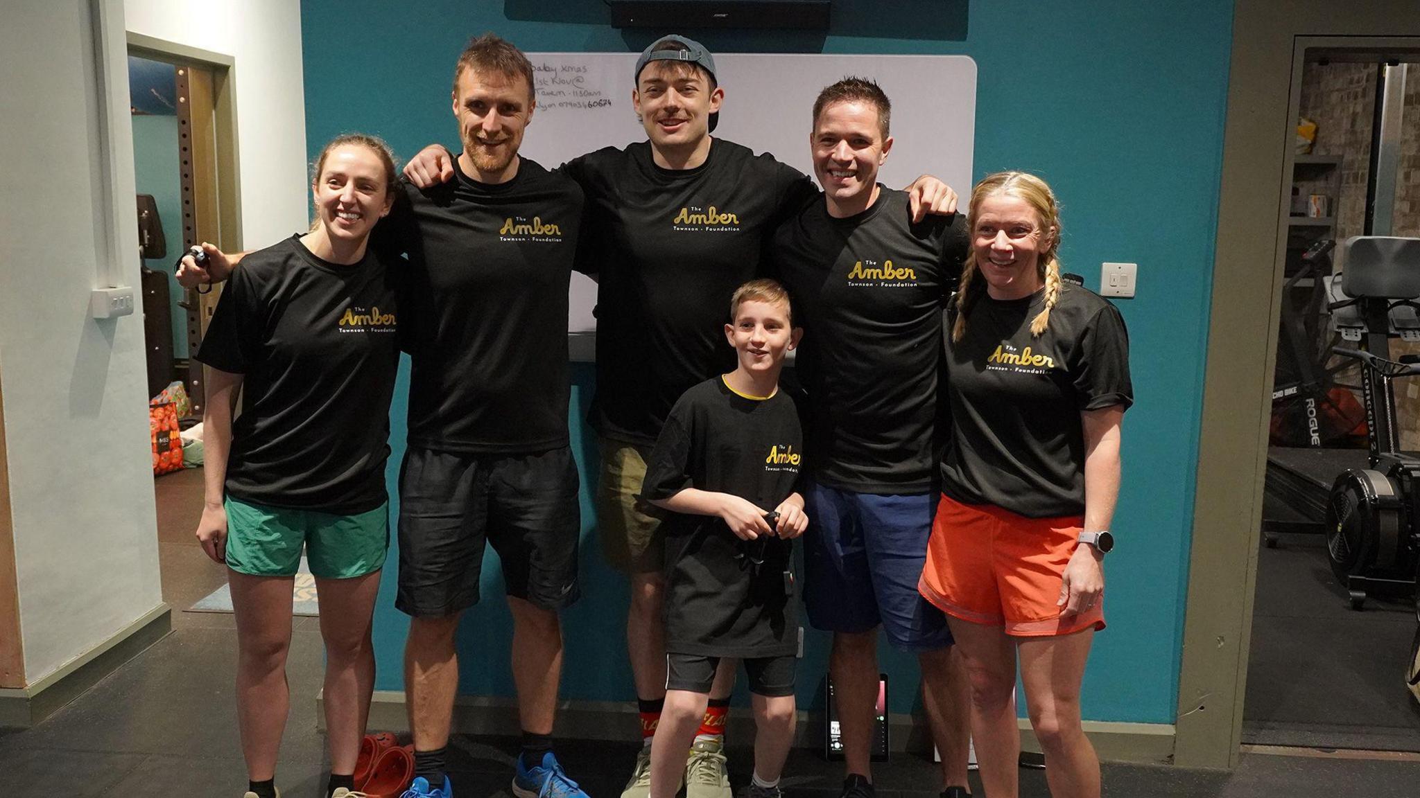 The group of six box steppers standing together with their arms around each other. They are wearing black shirts and are smiling at the camera.