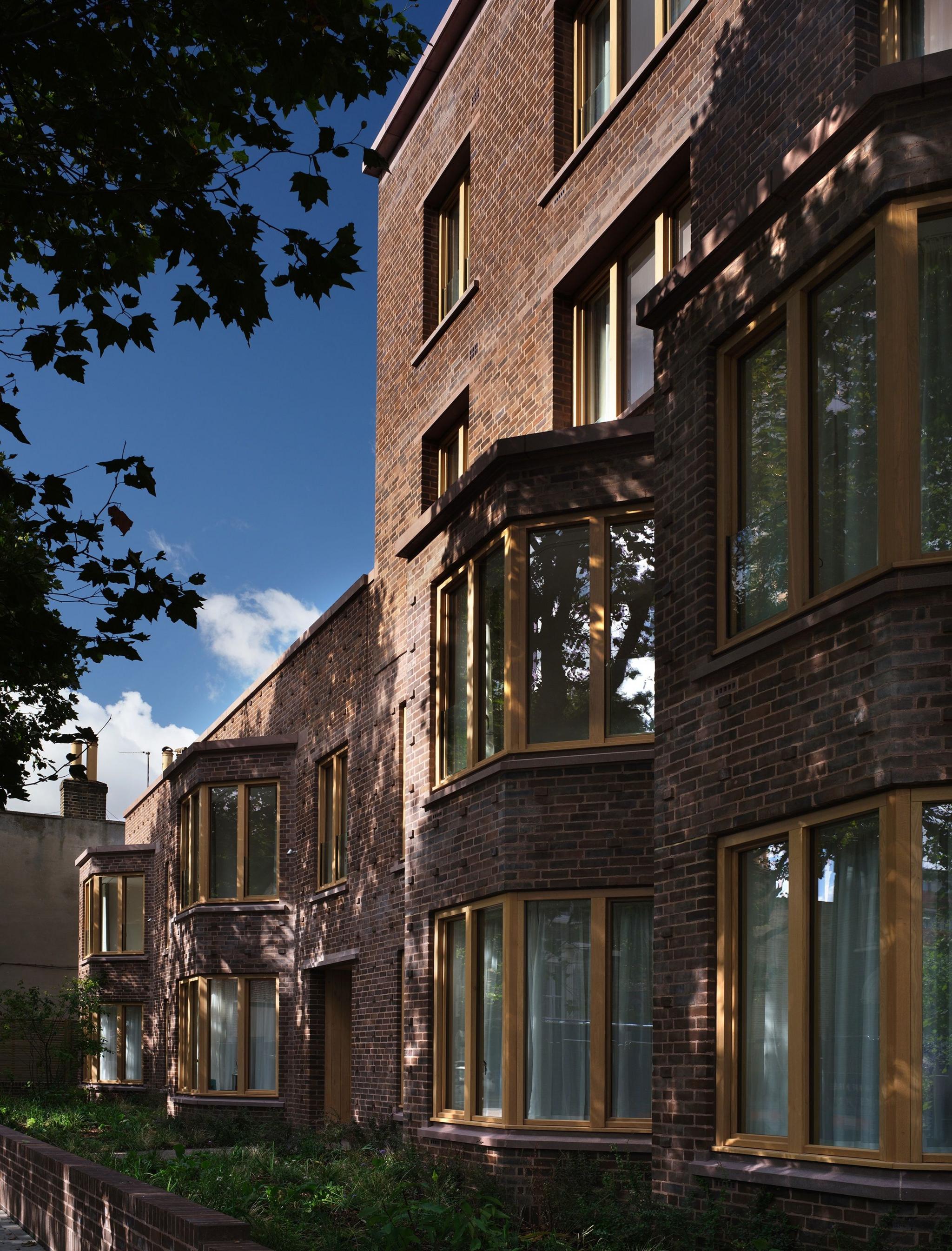 Exterior brick wall with a row of bay windows, evoking the traditional almshouse style
