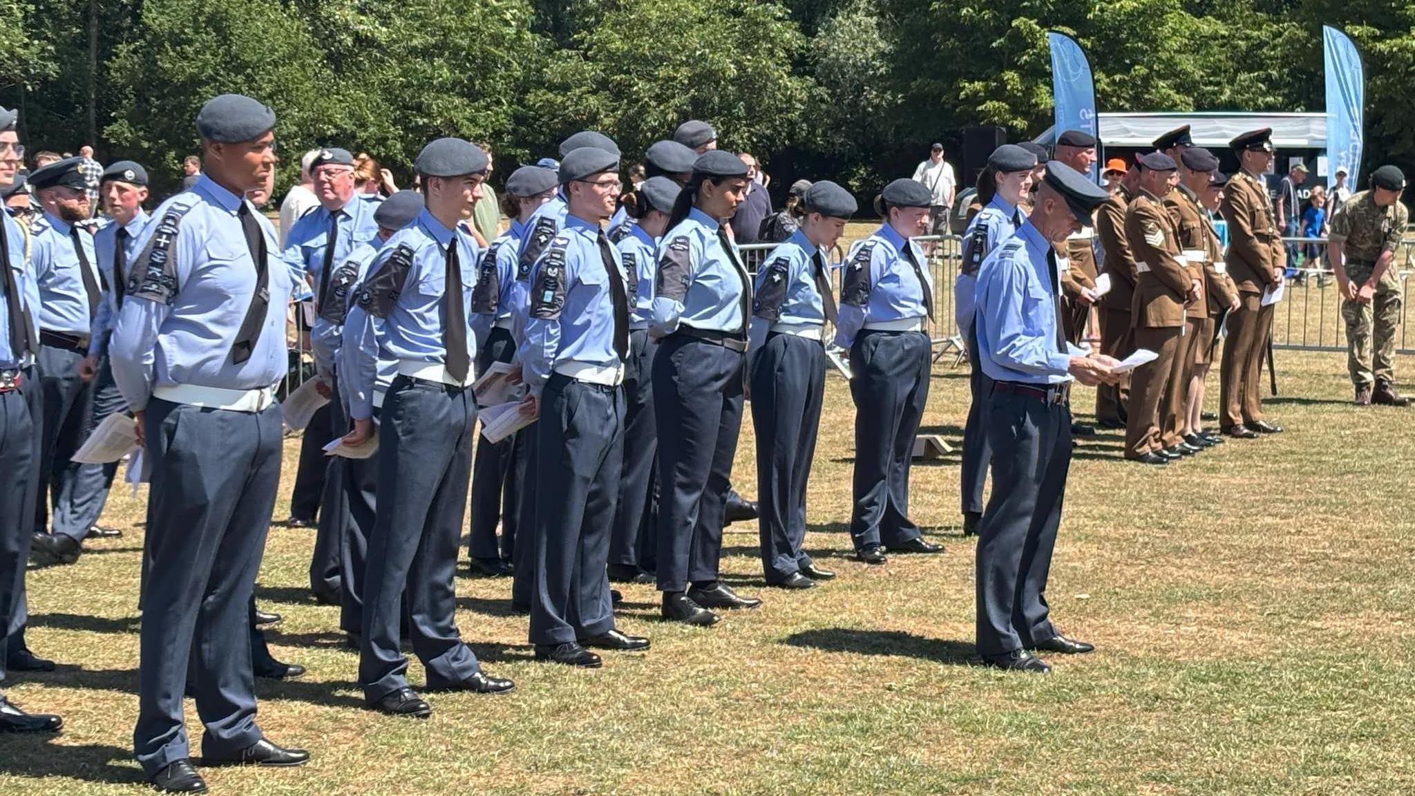 Military personnel in formation with one stood in front of the others reading from paper.