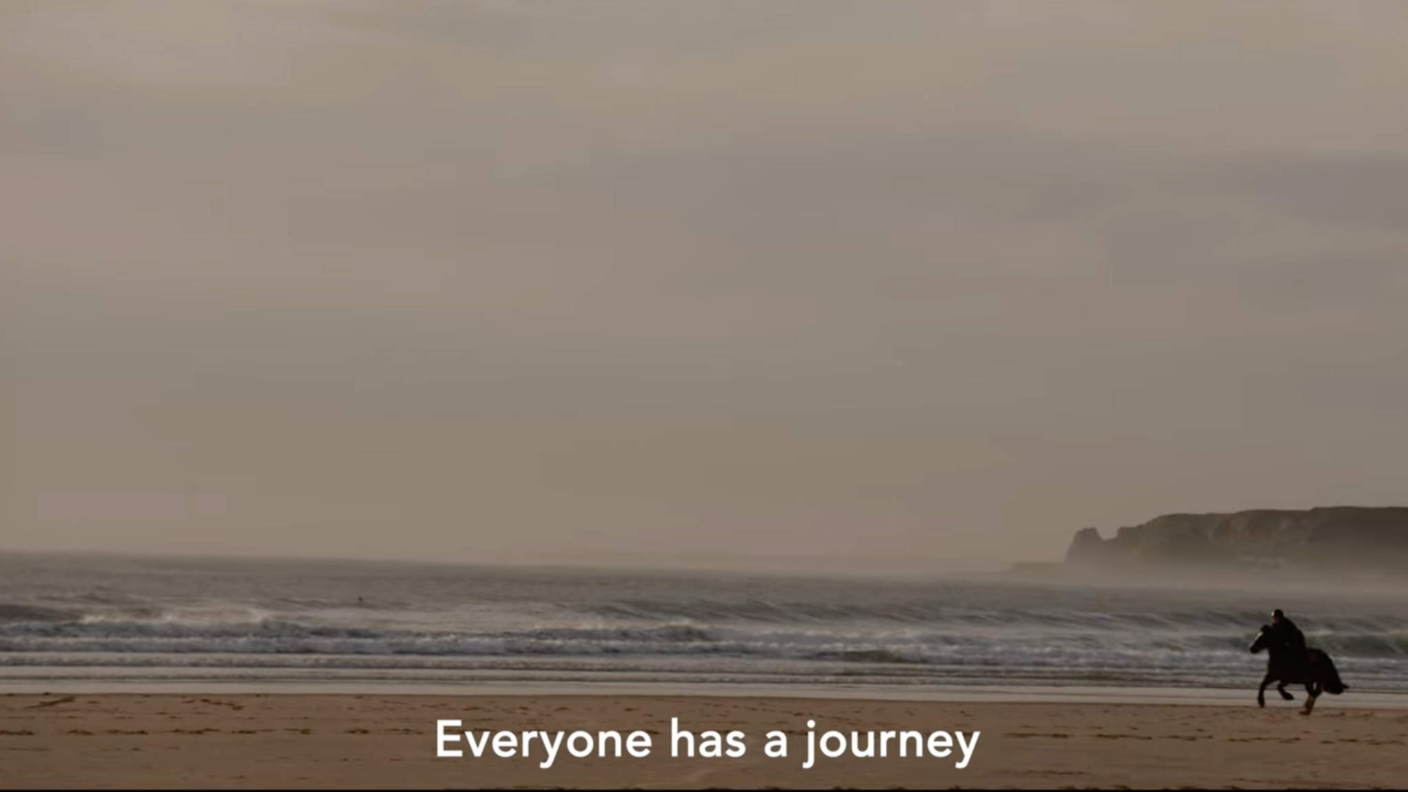 A shot from Lé Viage with a horse running along the beach at St Ouen's Bay. Subtitles say: "Everyone has a journey."