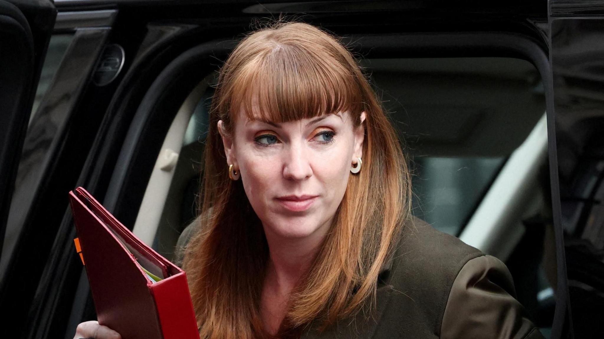 Angela Rayner, holding a red folder, steps out of a black car.