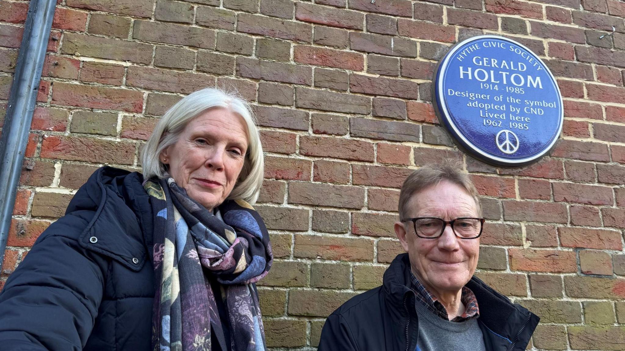 A man and a woman stood next to a blue plaque attached to a wall