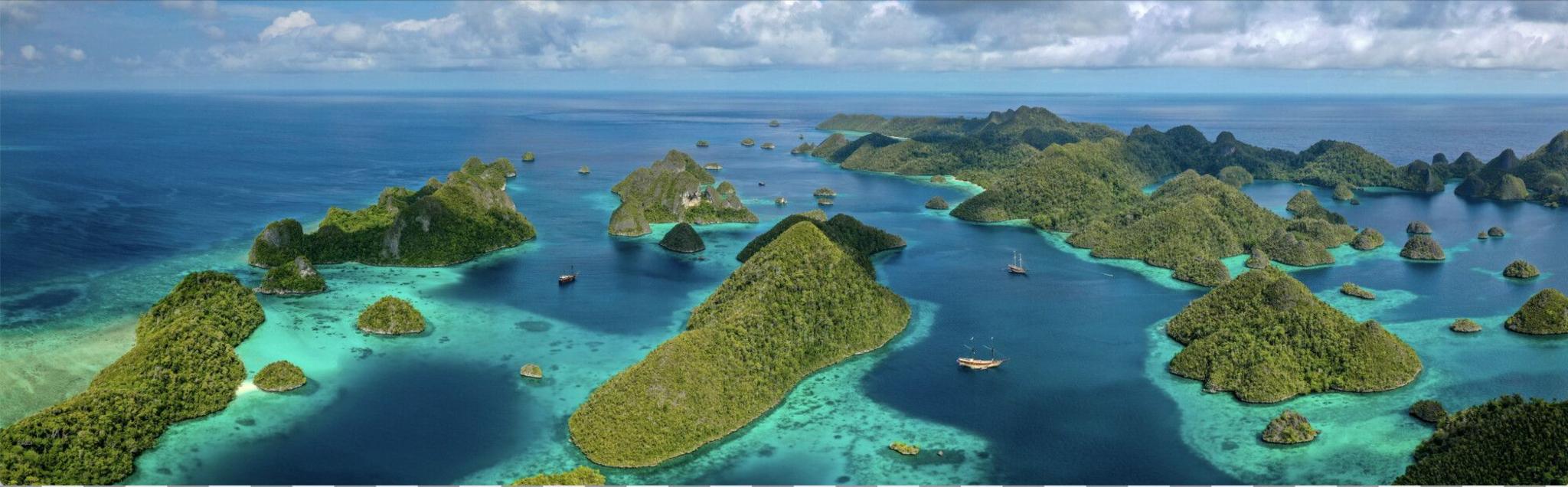 The aerial image shows dozens of tree-covered limestone peak islands in turquoise blue seas. This is Wayag, in Raja Ampat, which is a tourism hotspot.