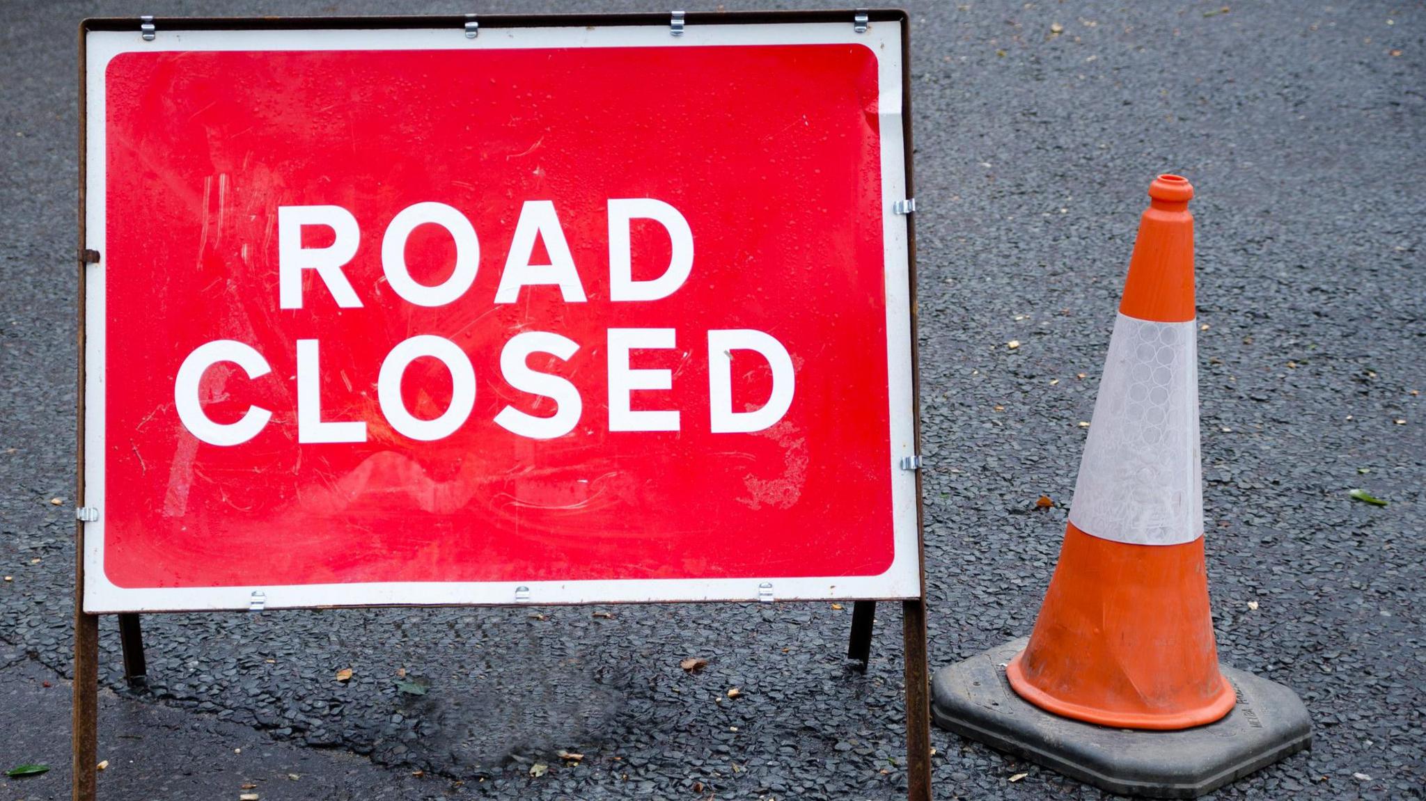 A road closed sign next to a traffic cone