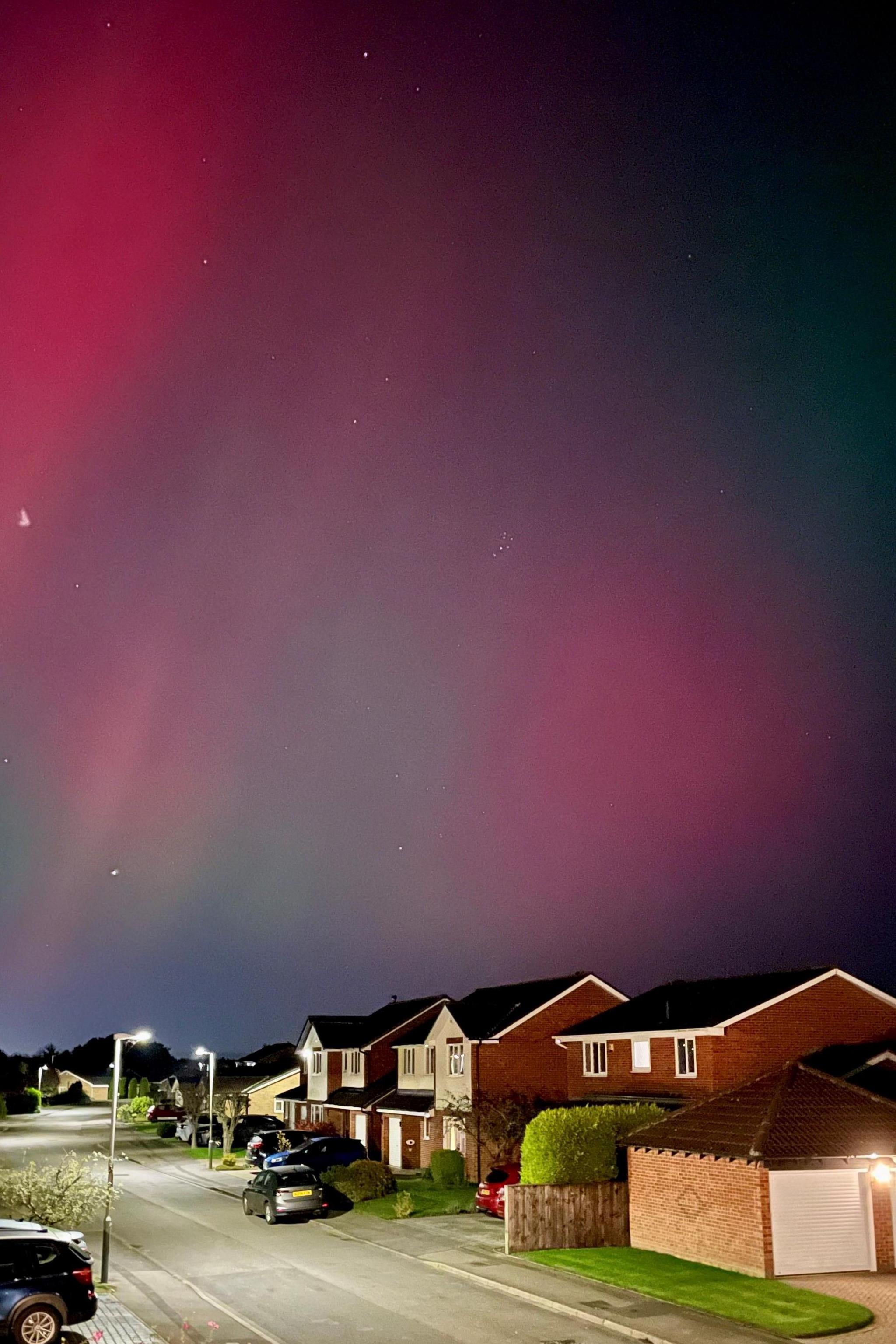 Red and purple skies above a street lined with houses. Cars are parked outside some of the properties.