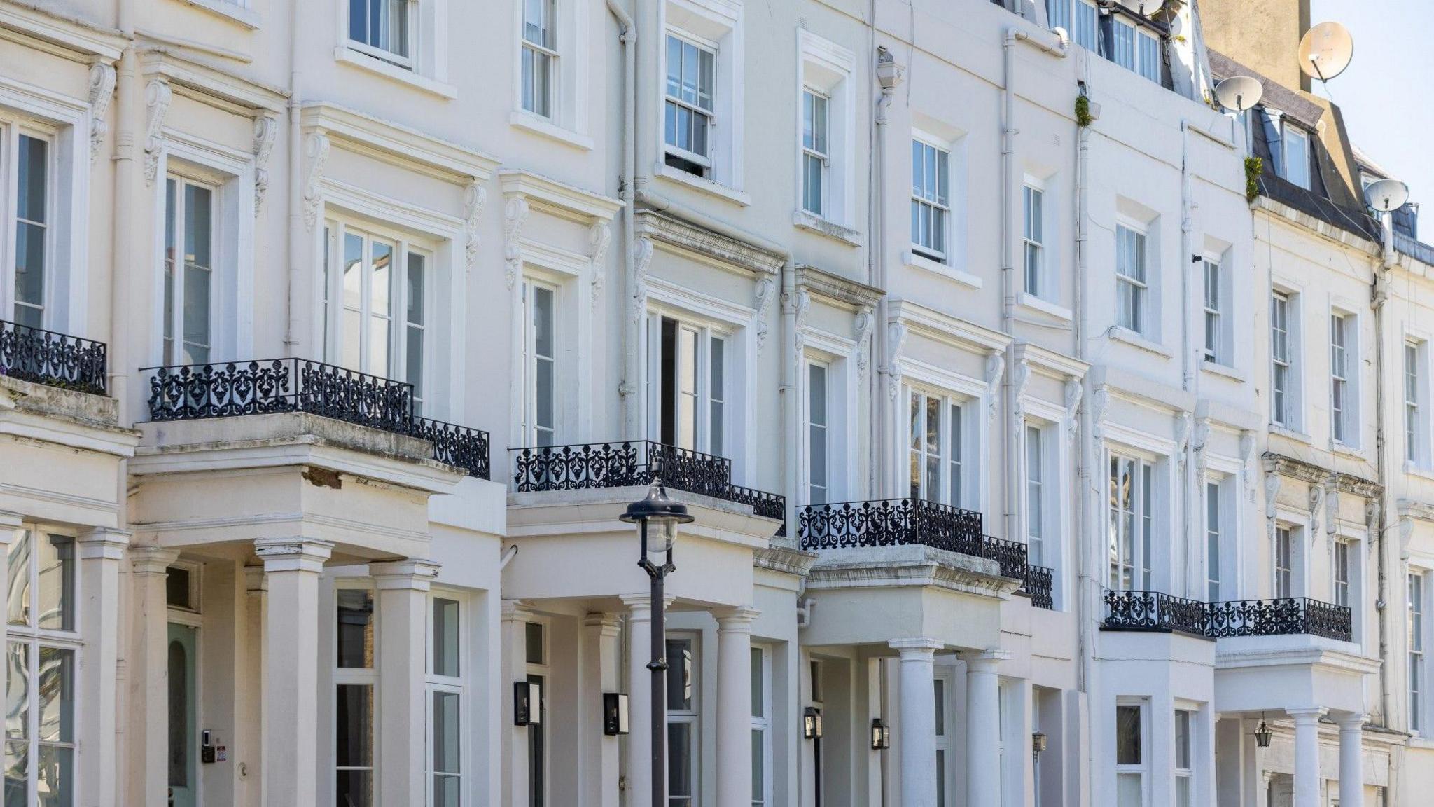 A stock image of a row of white houses with porticos at each entrance and small black railings above each one.