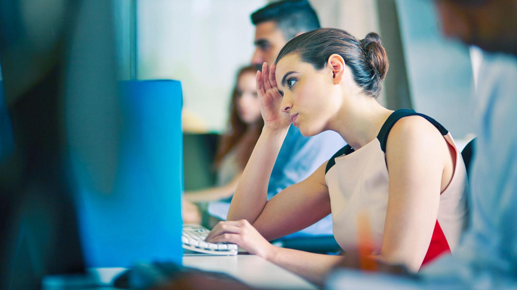 Office worker sitting at her computer looking stressed.