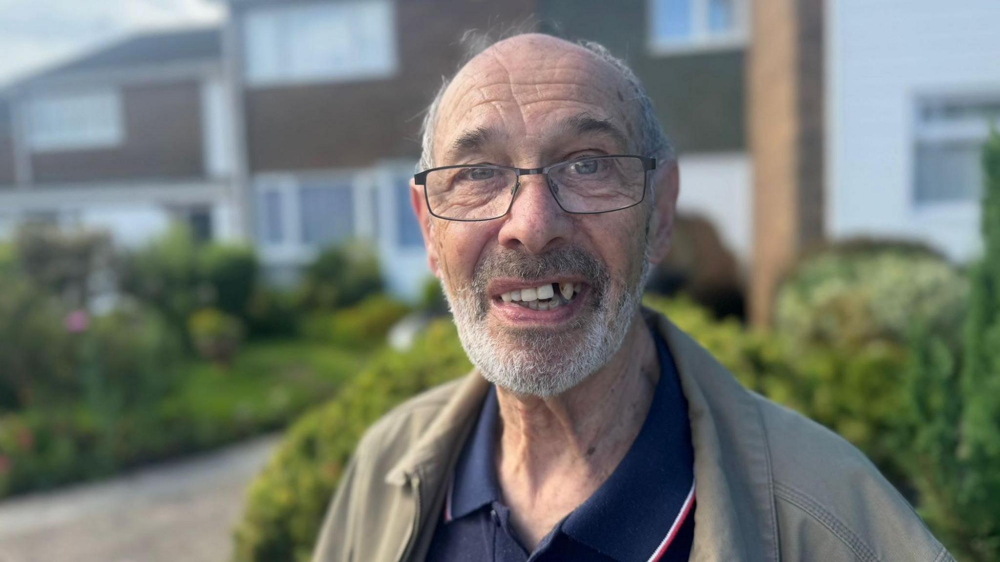 Micky Krause, standing outside, wearing glasses and wearing a beige jacket