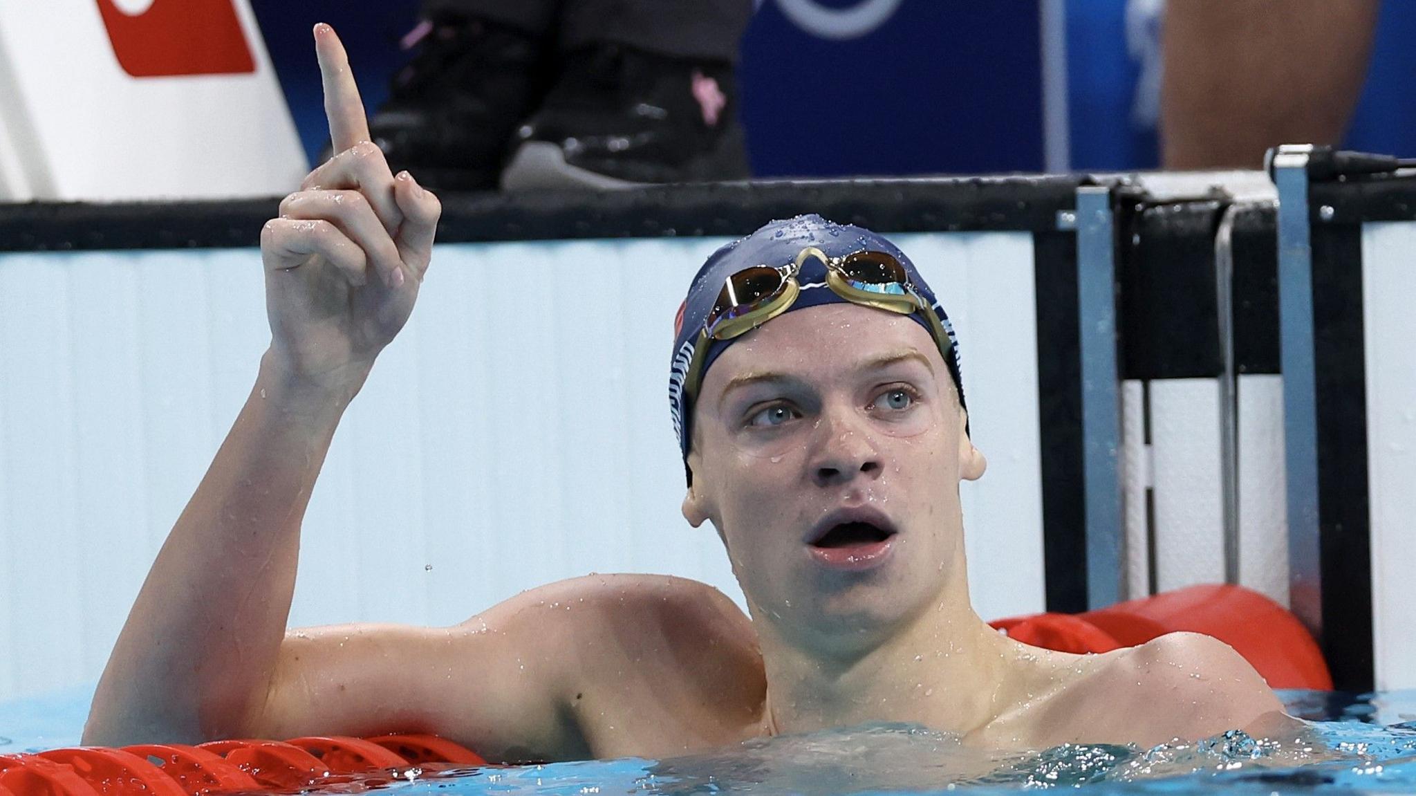 France's Leon Marchand, in the pool, raises a finger in celebration after winning an Olympic swimming gold