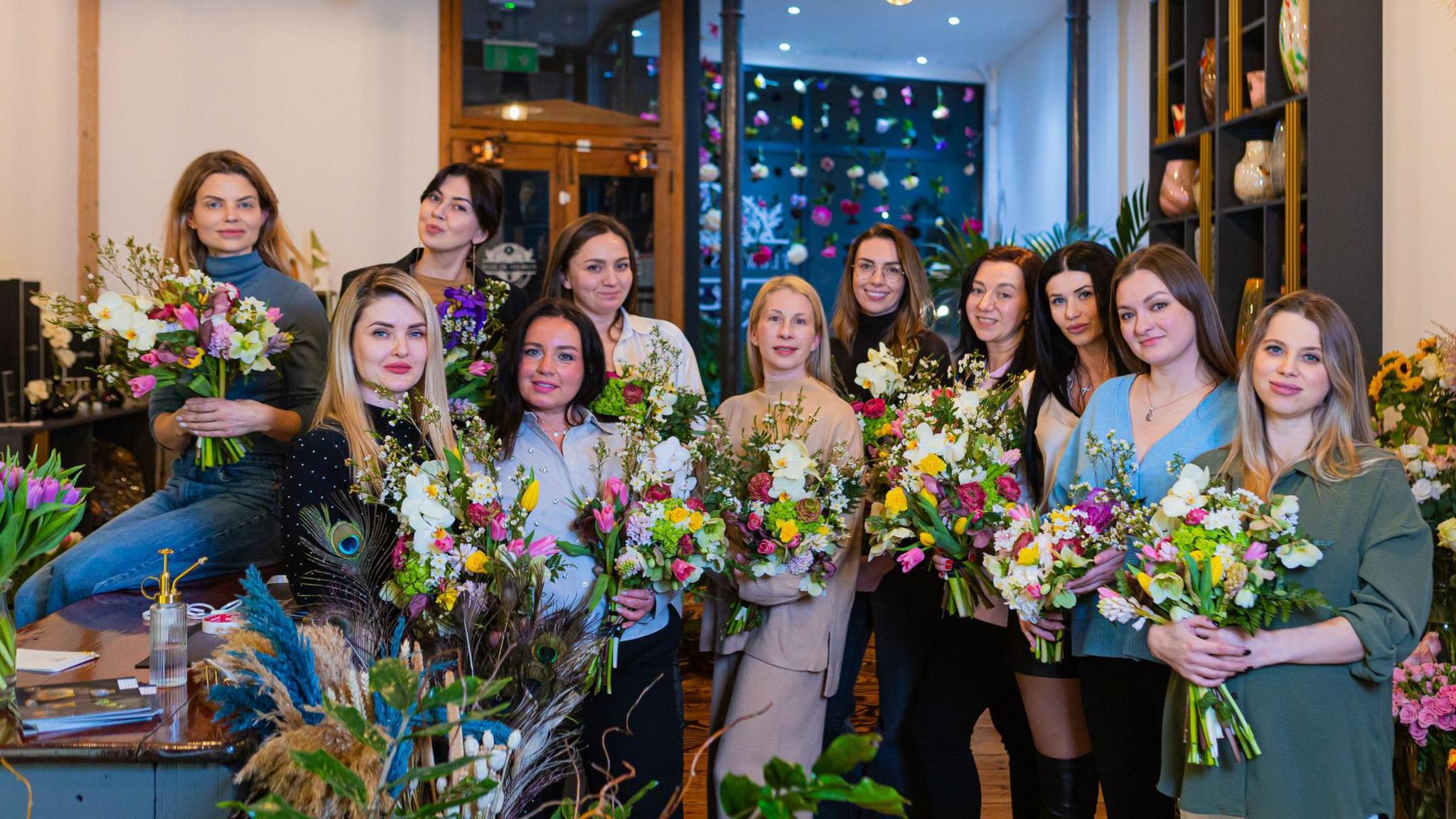 A group of 11 women who took part in a floristry session at a florists in Totterdown in Bristol hold up their floral creations as they pose for the camera