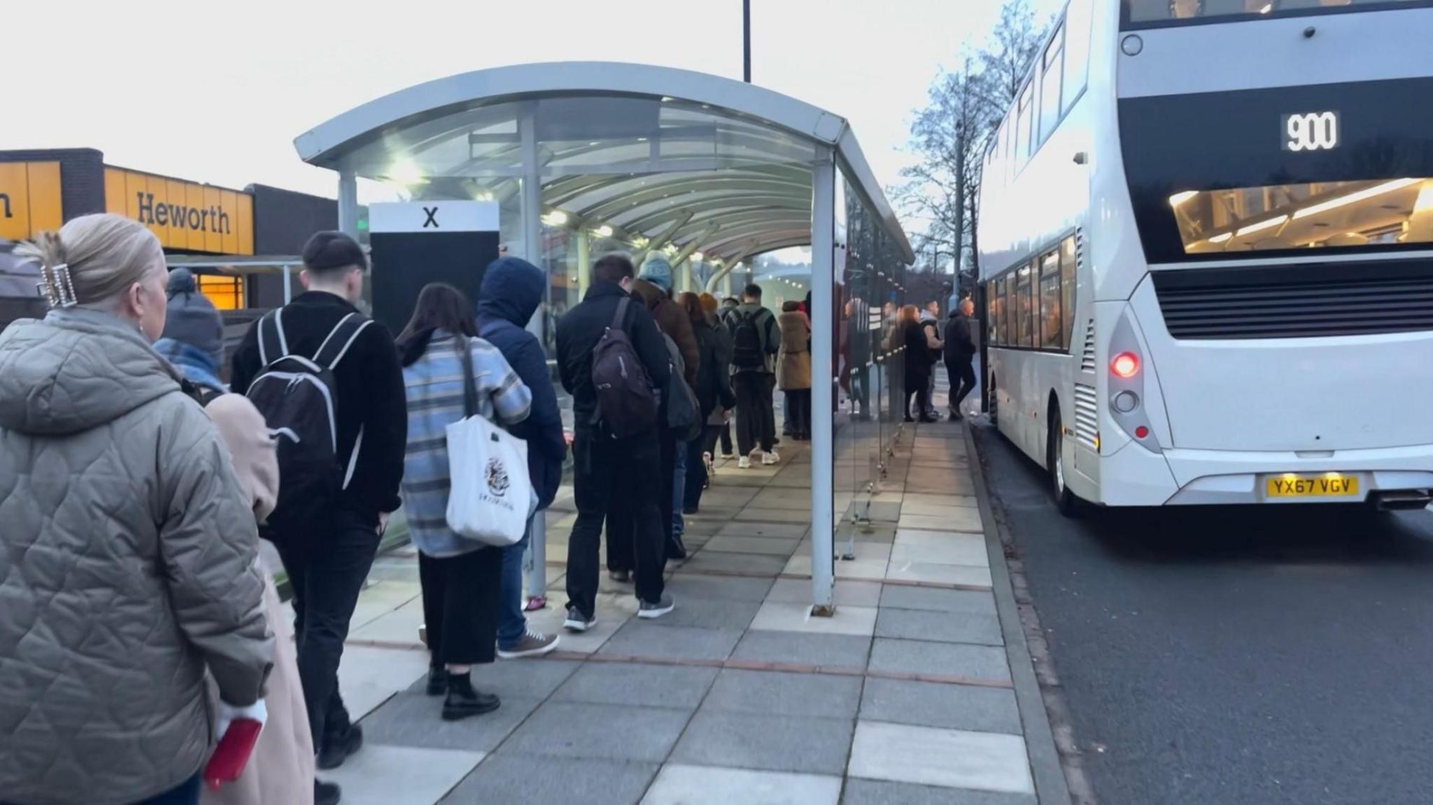 A queue of people wait at a bus stop outside Heworth Metro station.