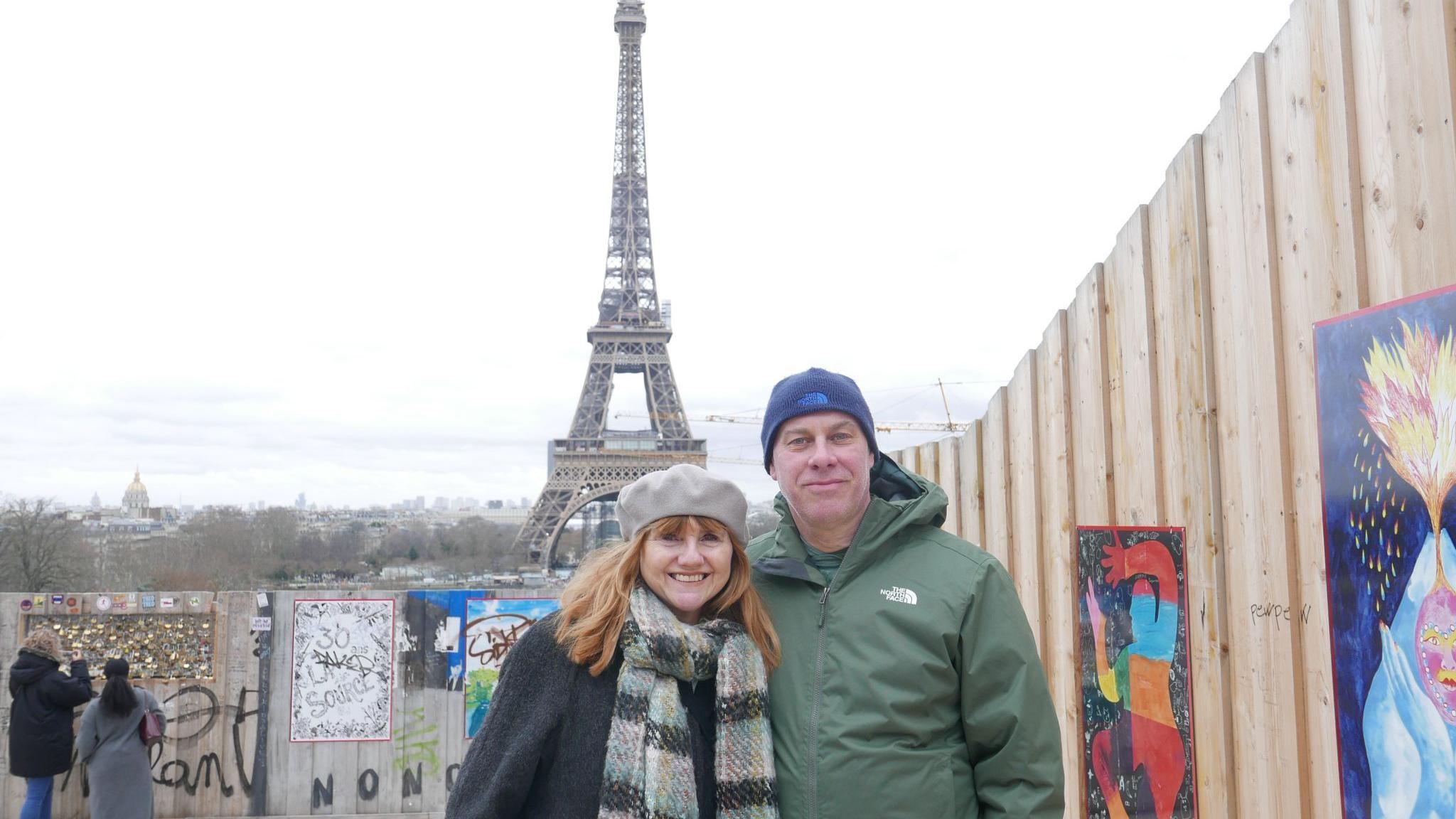 Phillipa and John Starns in winter coats and hats standing posing in front of the Eiffel Tower in Paris