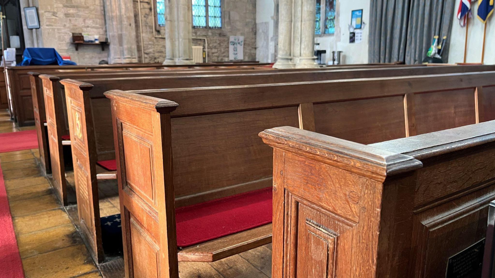 Wooden pews with red seat pads. The church pillars can be seen in distance.