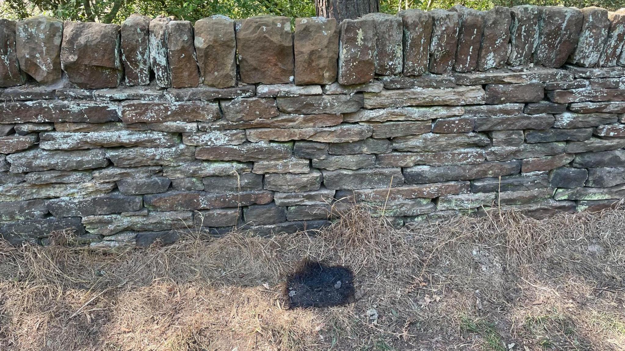 A black rectangular shape of scorched earth on the grass