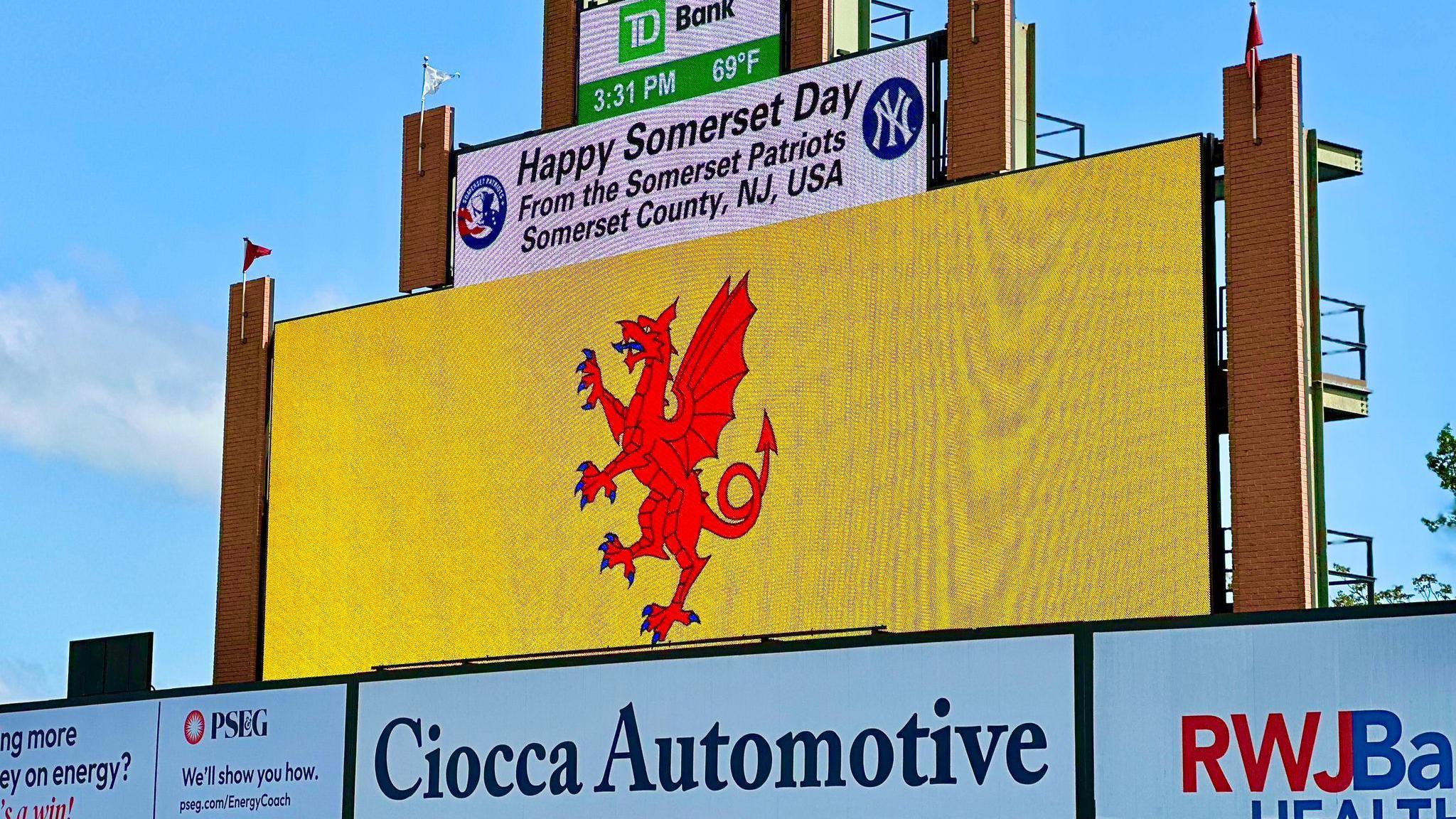 The Somerset flag is displayed on a digital screen at a Baseball game. Over it a message reads Happy Somerset Day from the Somerset Patriots.