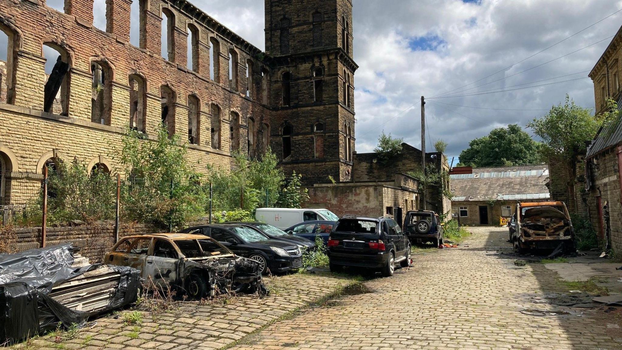 A row of burnt out cars at the back of the burnt out Genappe Mill building  