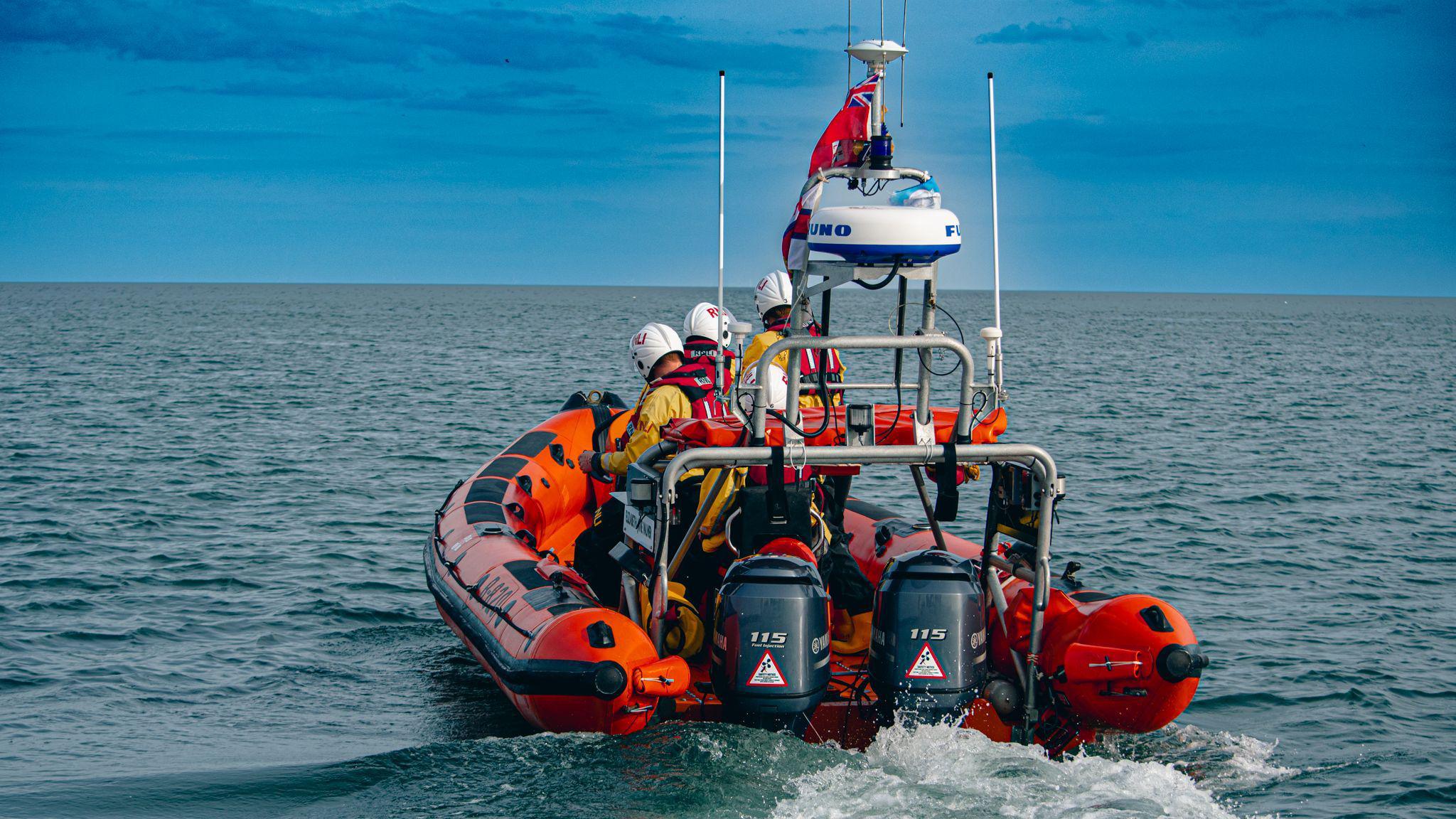 A lifeboat heading through the sea with the backs of three crew members visible