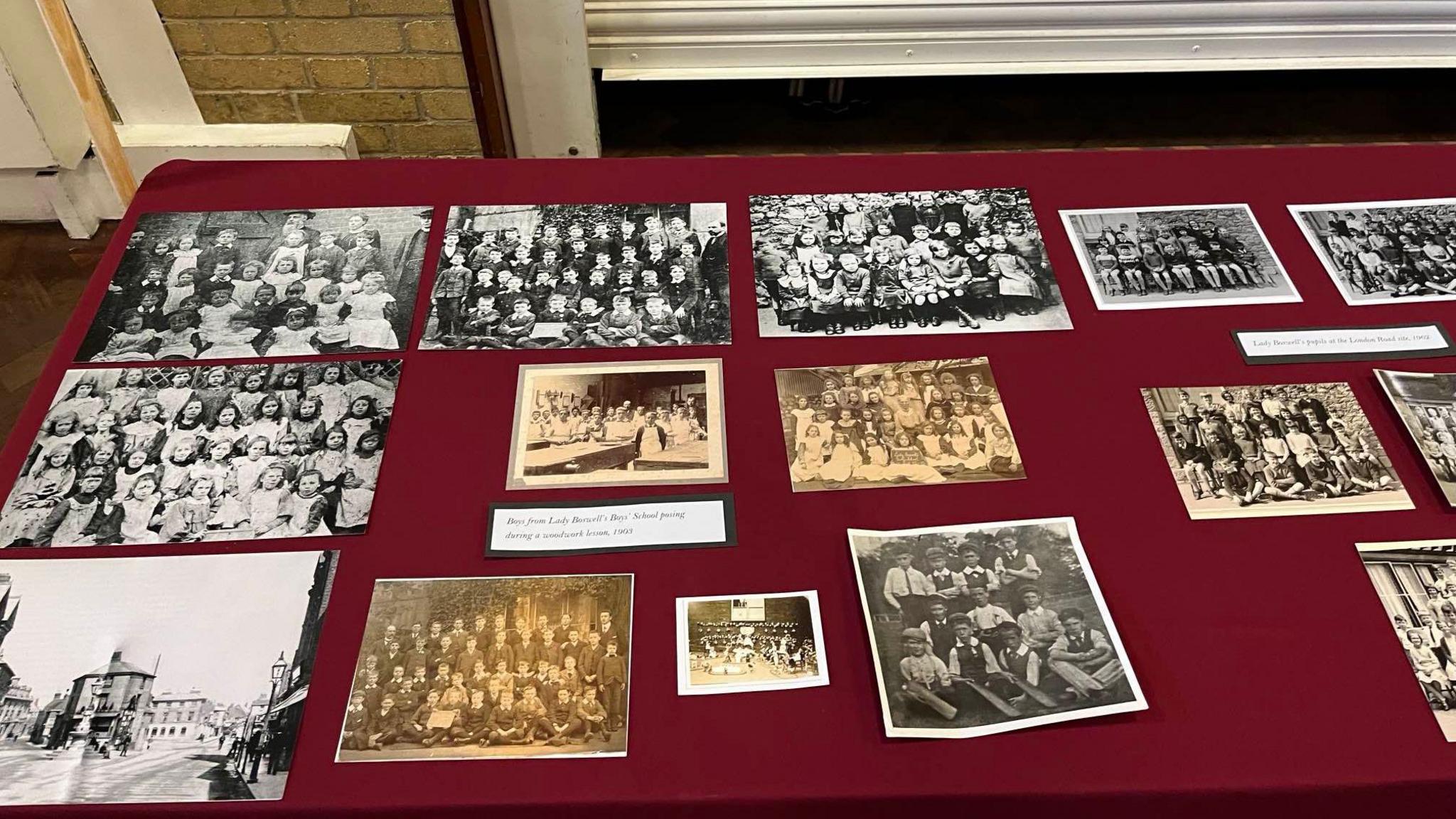 A selection of black and white photographs of school children laid out on a red table cloth