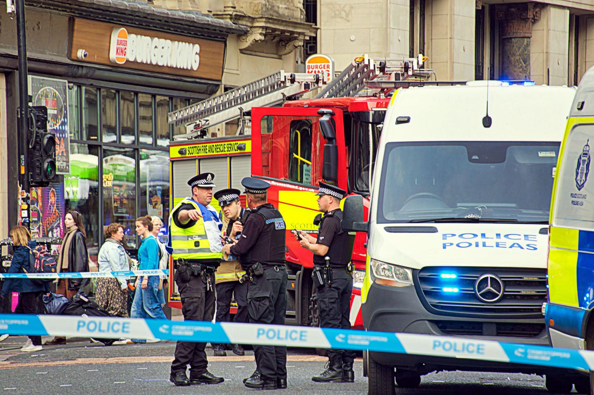 Police officers at the scene of the collision with police vans beside them and a fire engine also visible, all behind police tape