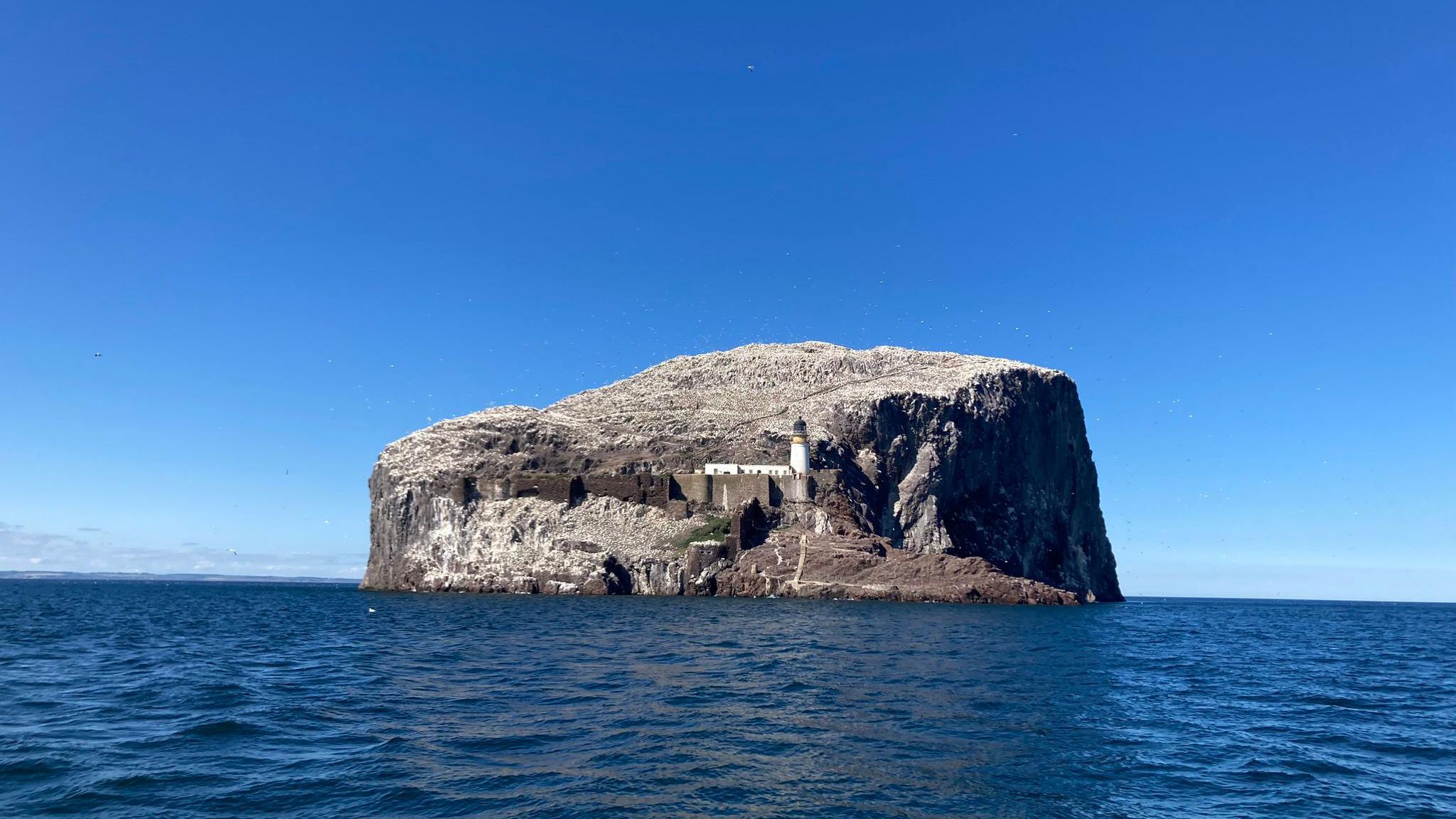 Bass Ross in the distance, surrounded by a blue sky and dark blue water.